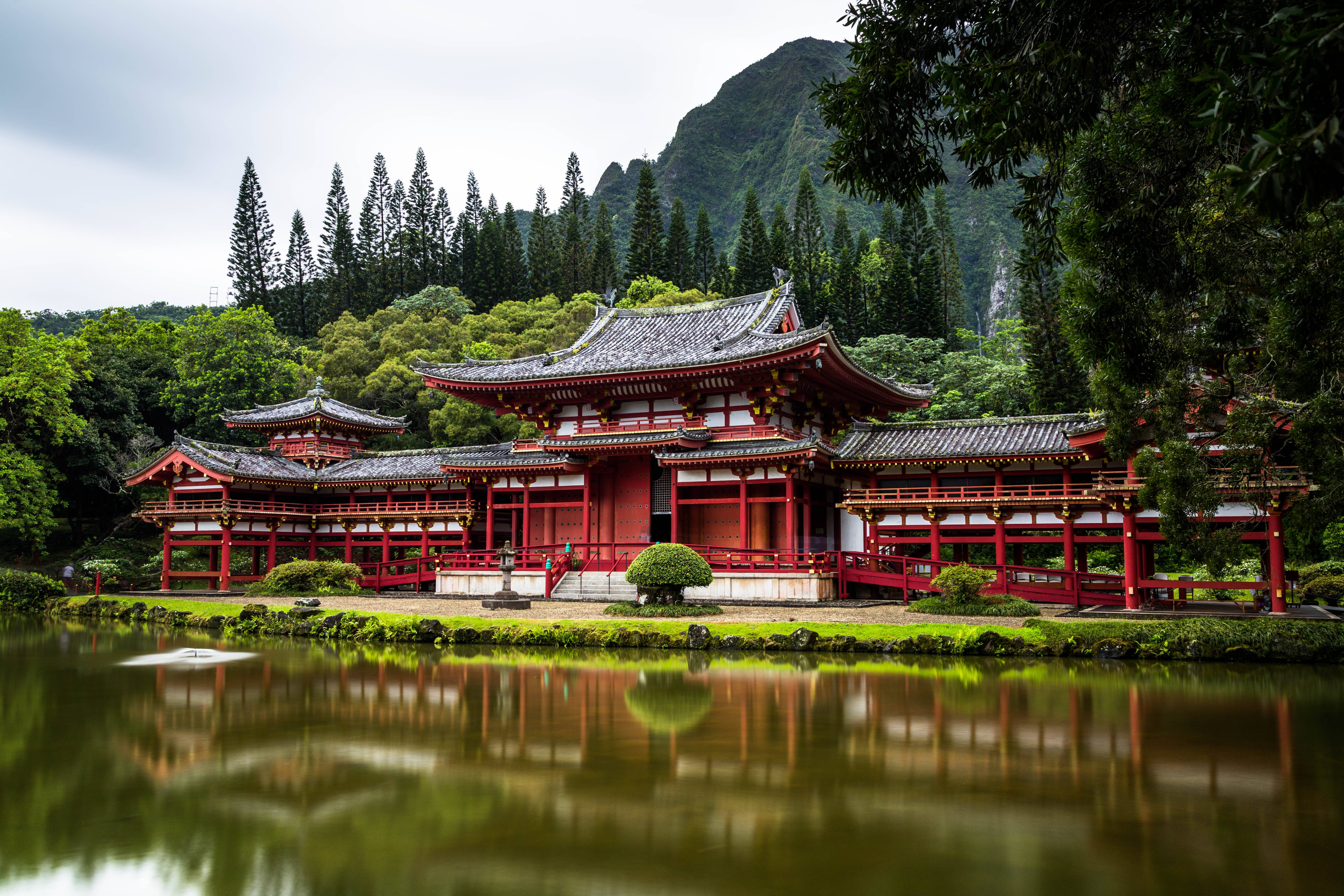 紅色日本寺廟倒映在寧靜的池塘中，背景是森林覆蓋的山脈。