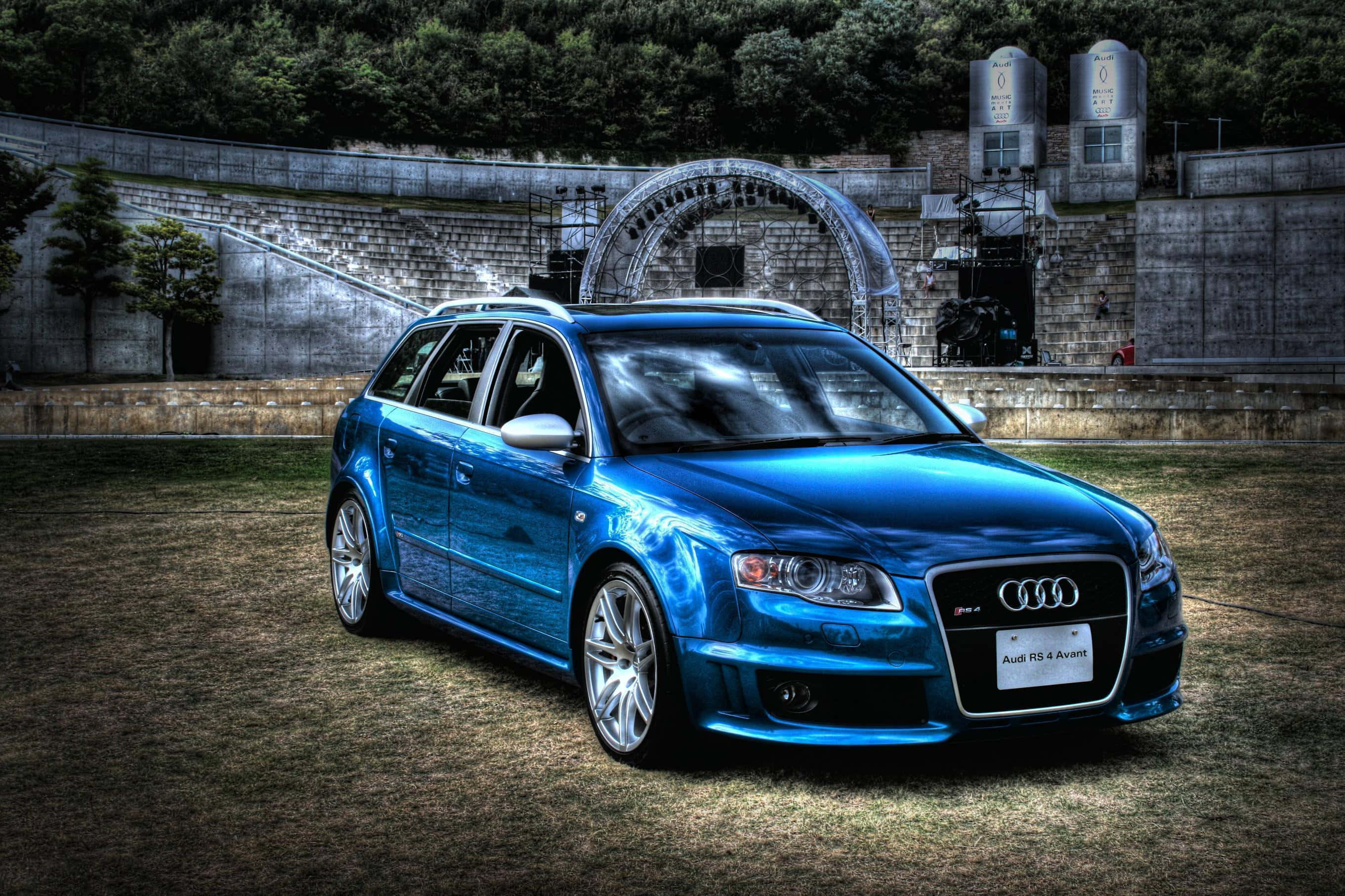 Audi Rs5 桌布 壁紙 — 一輛充滿活力的藍色 Audi RS4 Avant 旅行車在石頭圓形劇場附近的草地上，在戲劇性的燈光下閃閃發光。