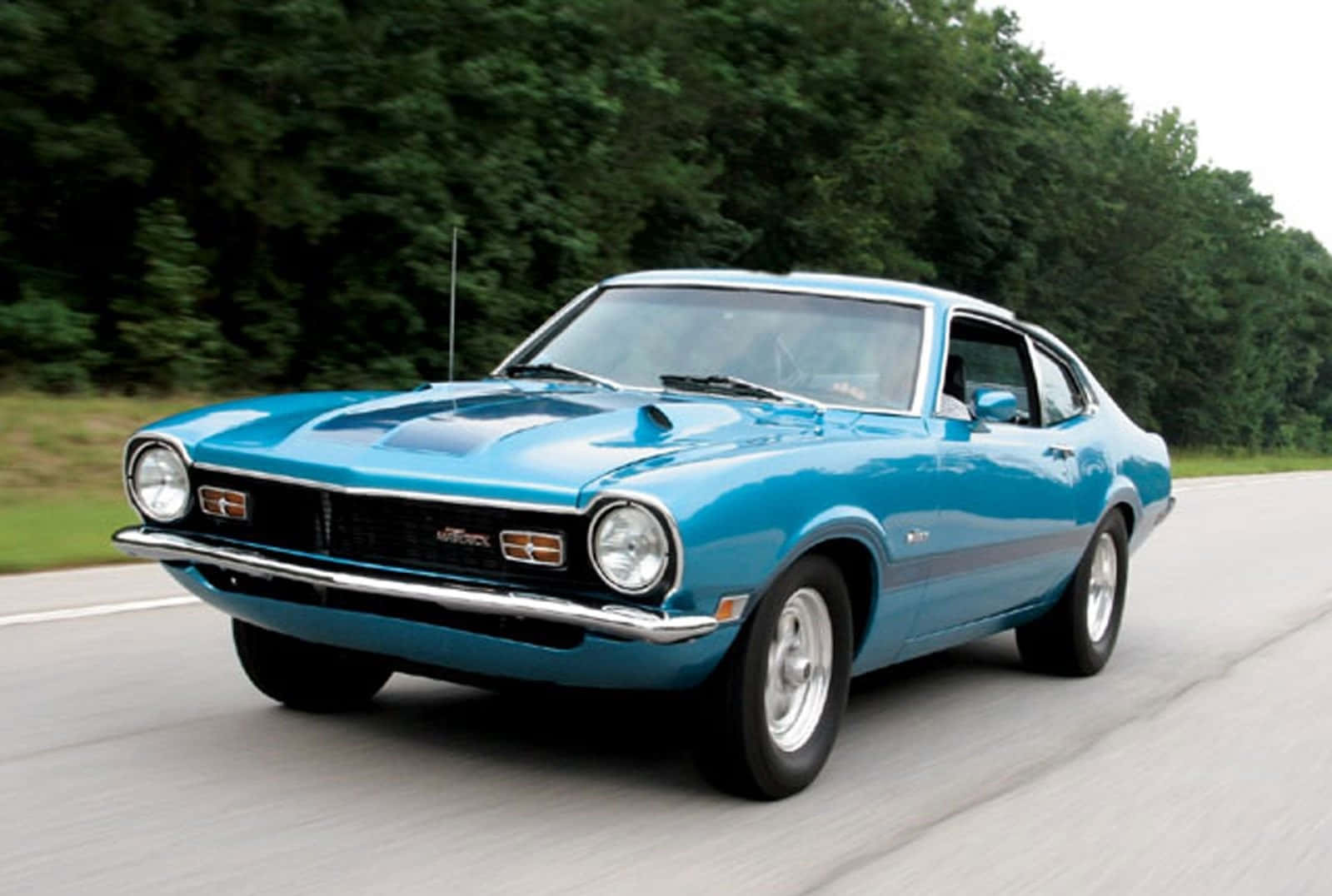 Ford Maverick 桌布 壁紙 — 一輛充滿活力的藍色經典肌肉車在樹木成蔭的道路上奔馳，動態模糊傳達出力量與自由。