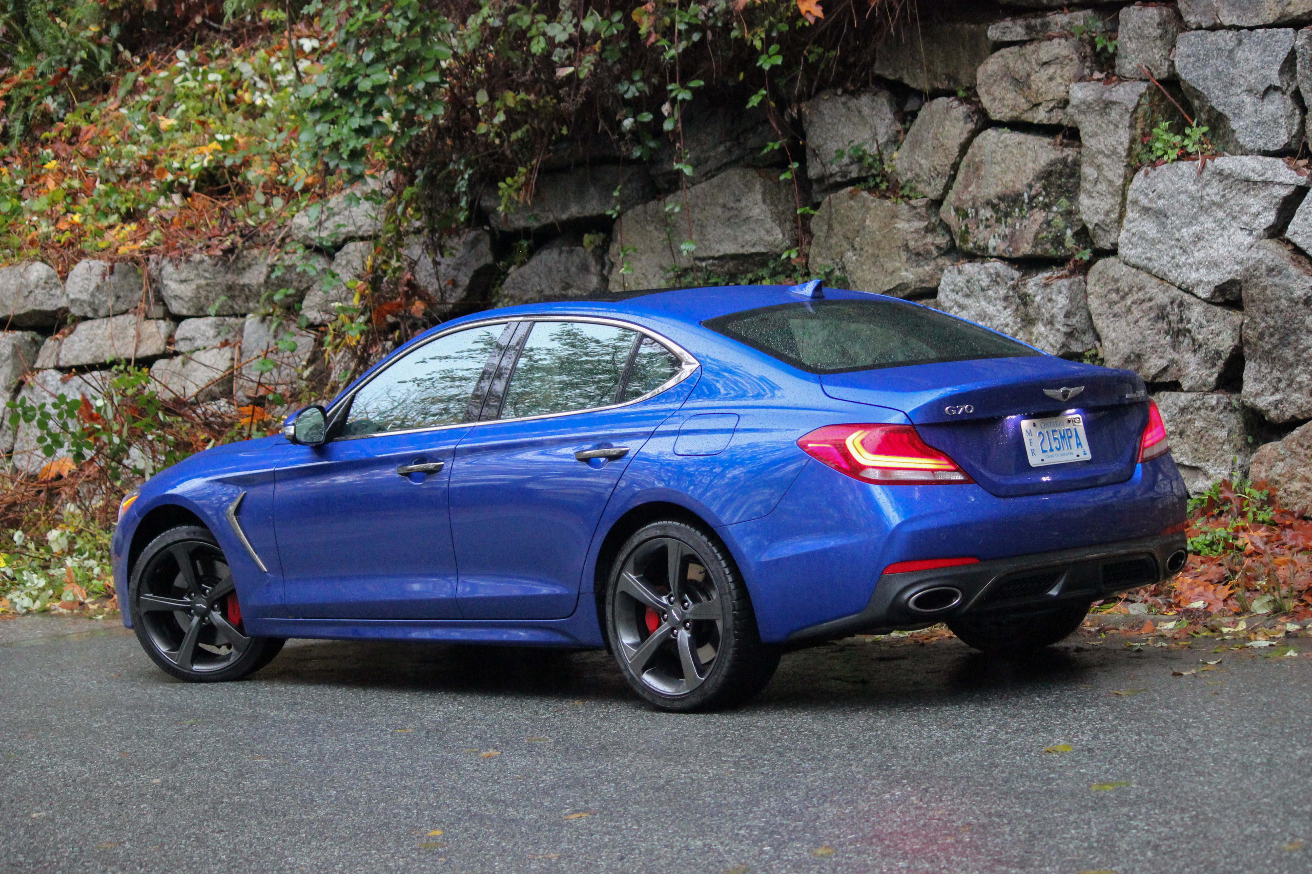 Genesis G70 桌布 壁紙 — 一輛充滿活力的藍色 Genesis G70 運動轎車停在潮濕的路面上，旁邊是長滿青苔的石牆，正值秋季。