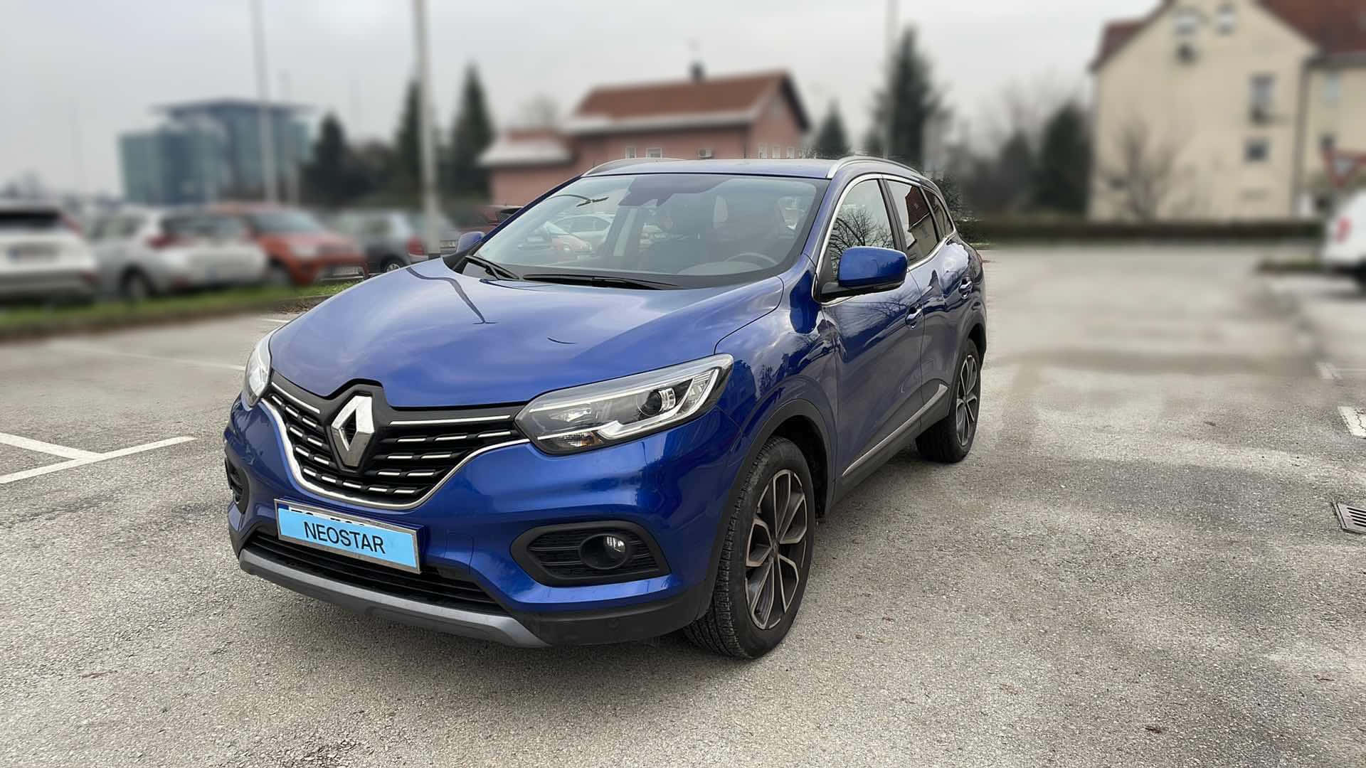  壁紙 — 一輛鮮藍色的雷諾Kwid SUV停泊在灰色瀝青停車場，背景有模糊的建築物和樹木。