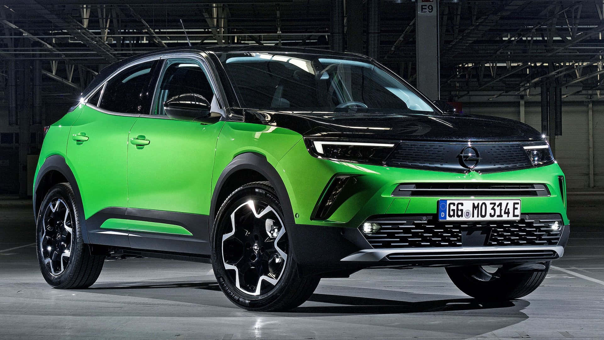 Opel Mokka 桌布 壁紙 — 一輛充滿活力的綠色和黑色電動SUV在一個寬敞的工業倉庫中展示，倉庫有高天花板和裸露的橫樑。