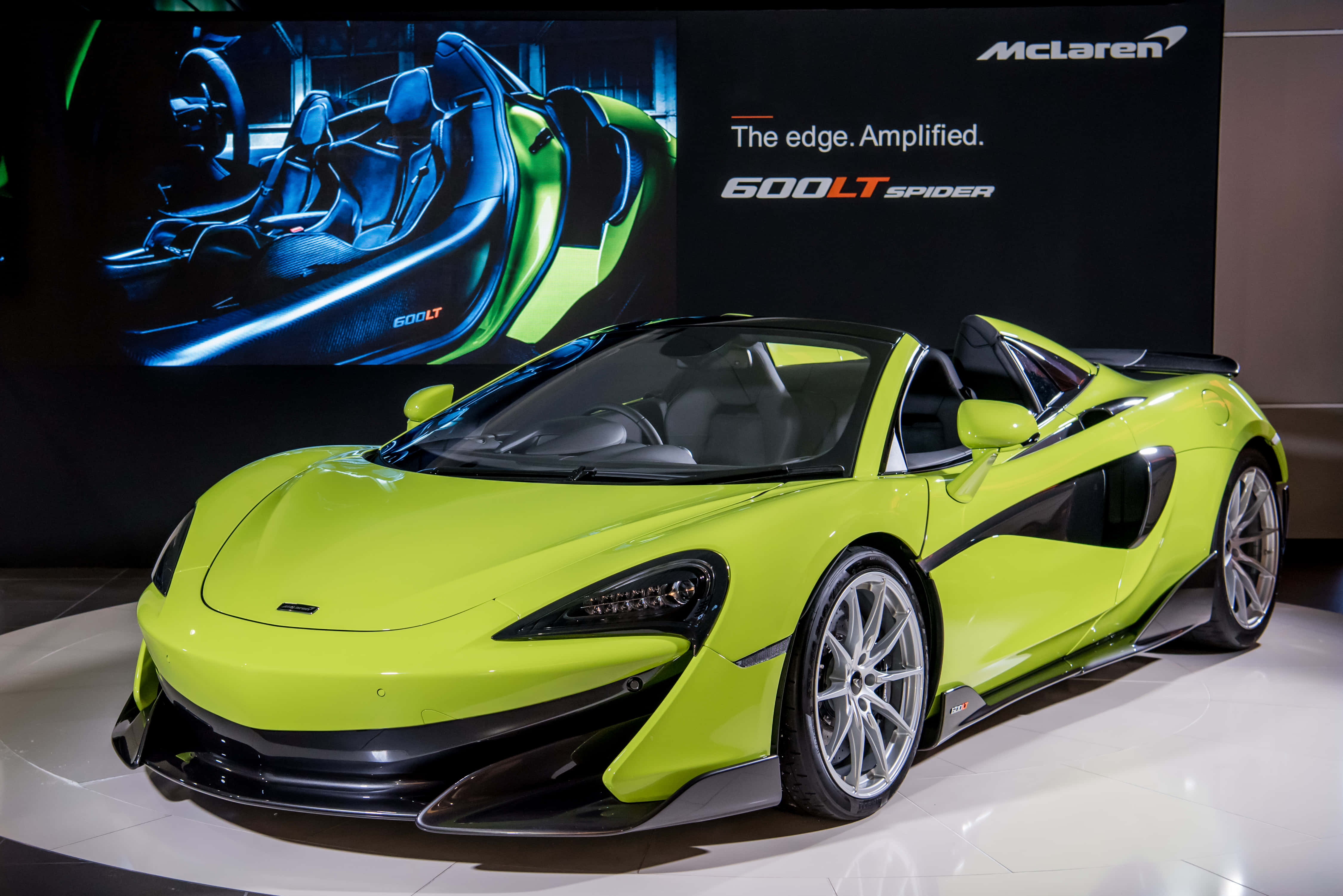 Mclaren 600lt Spider 桌布 壁紙 — 一輛充滿活力的青檸綠色McLaren 600LT Spider跑車在車展上，在明亮的燈光下閃閃發光，背景帶有品牌標誌。