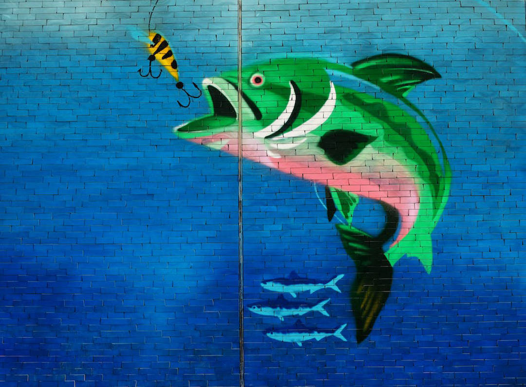 藍色磚牆上，一條跳躍的魚追逐魚餌的彩色壁畫。