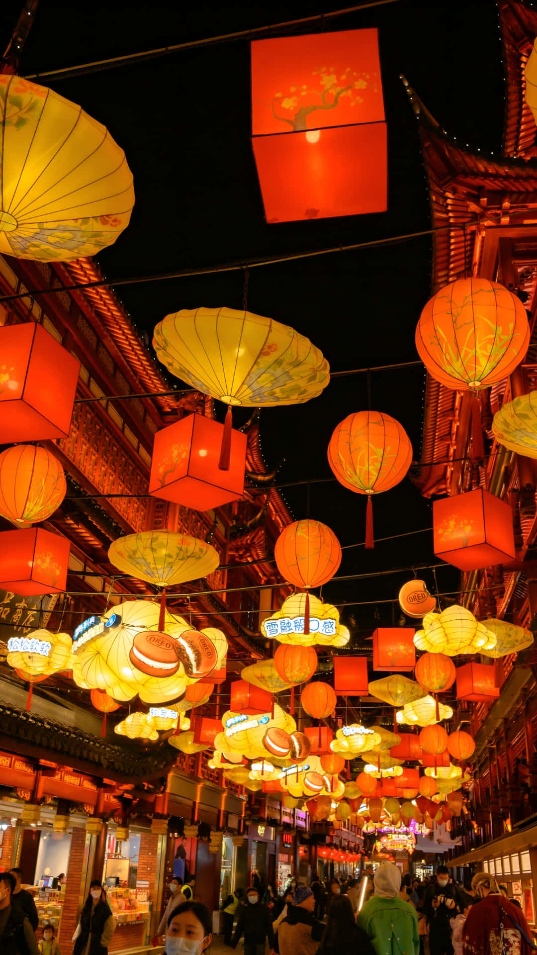  壁紙 — 一條充滿活力的夜晚街道，掛滿發光的紅色和黃色燈籠，懸掛在人群上方。