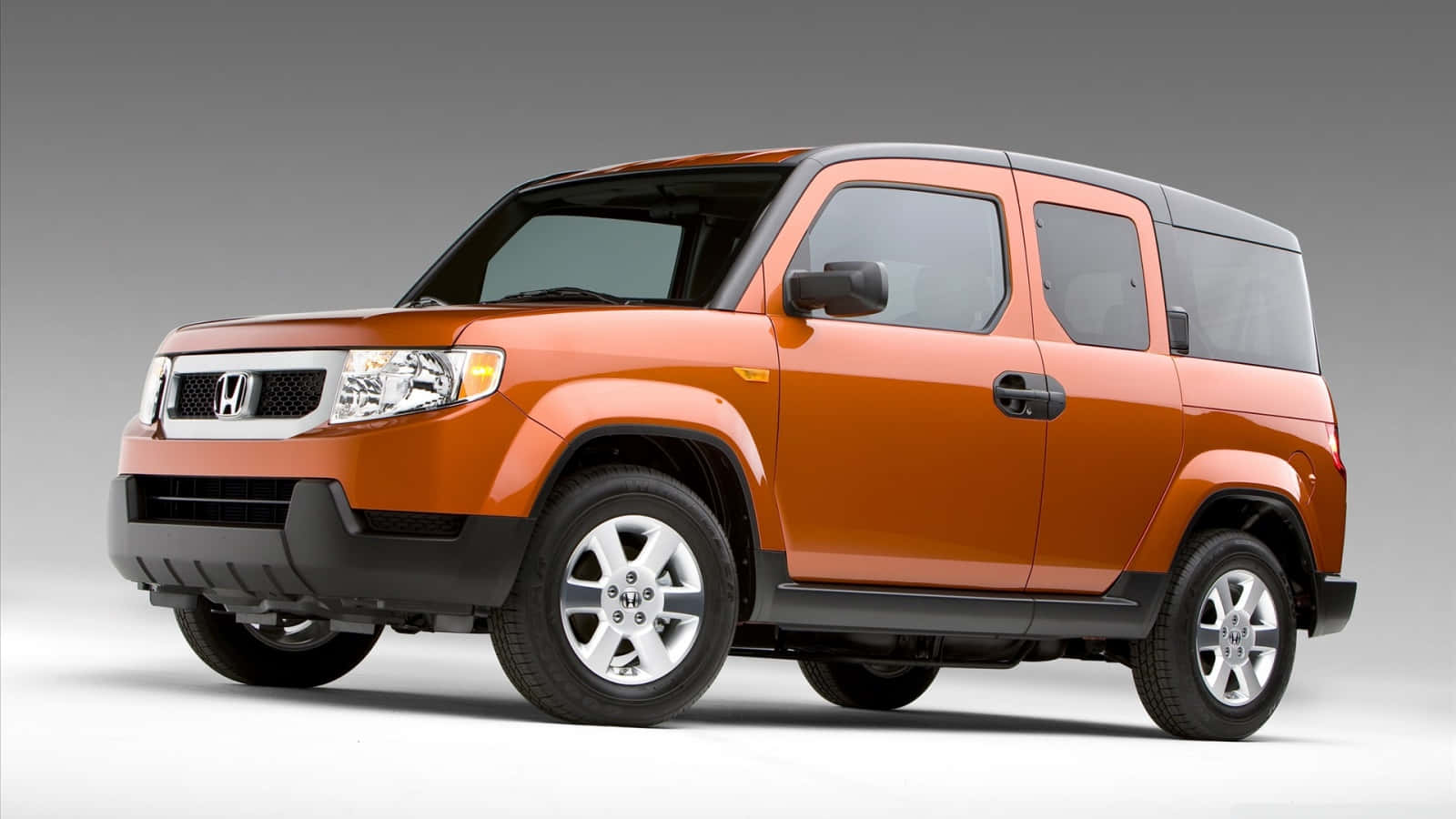 Honda Element 桌布 壁紙 — 一輛充滿活力的橙色本田 Element SUV，帶有黑色飾邊和銀色輪圈，矗立在乾淨的攝影棚環境中。