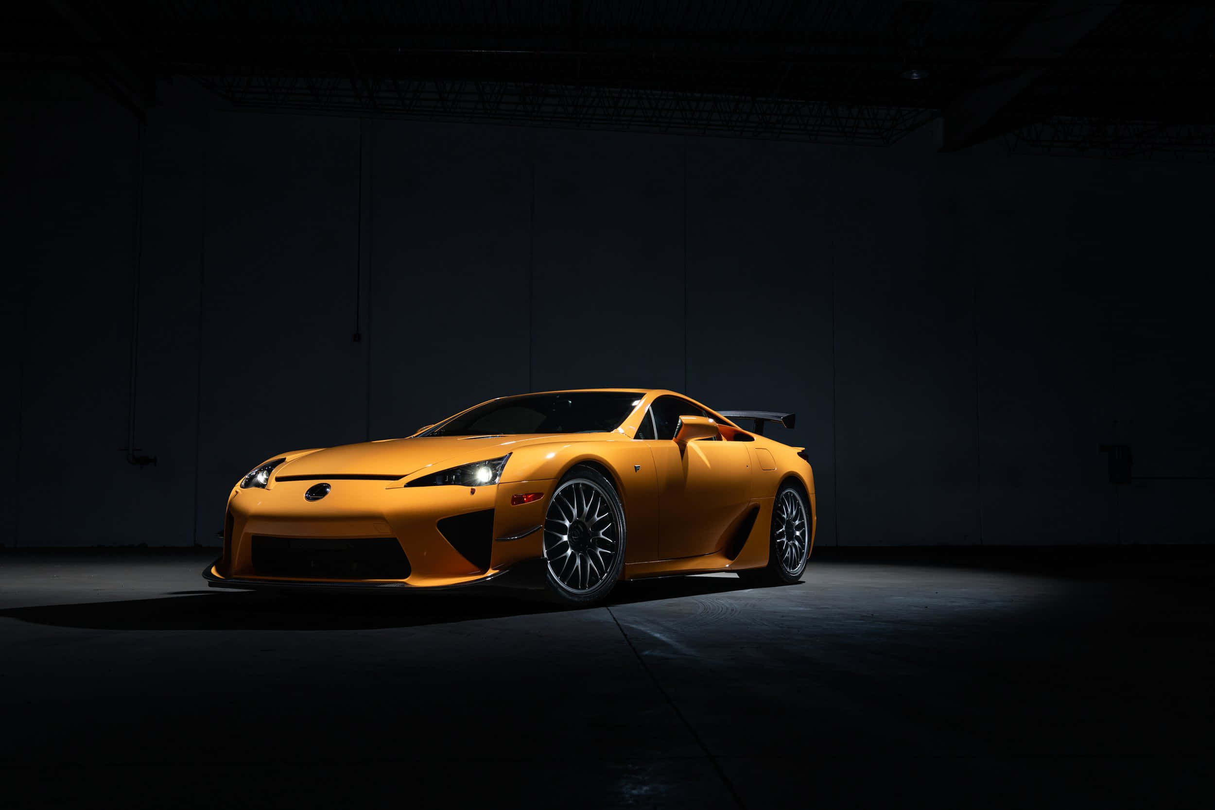 Lexus Lfa 桌布 壁紙 — 一輛充滿活力的橙色Lexus LFA跑車在黑暗的工業車庫中，在戲劇性的聚光燈下閃閃發光。
