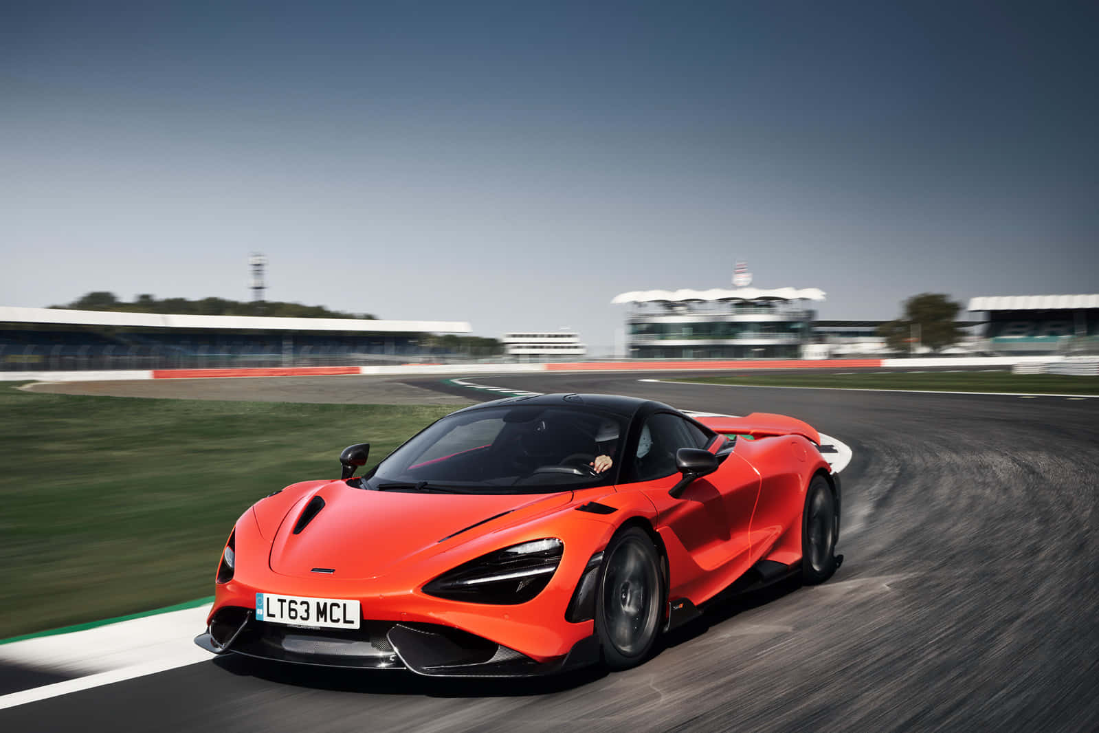 Mclaren 765lt 桌布 壁紙 — 一輛充滿活力的橙色McLaren 720S在賽道上疾馳，動態模糊效果凸顯其高性能。