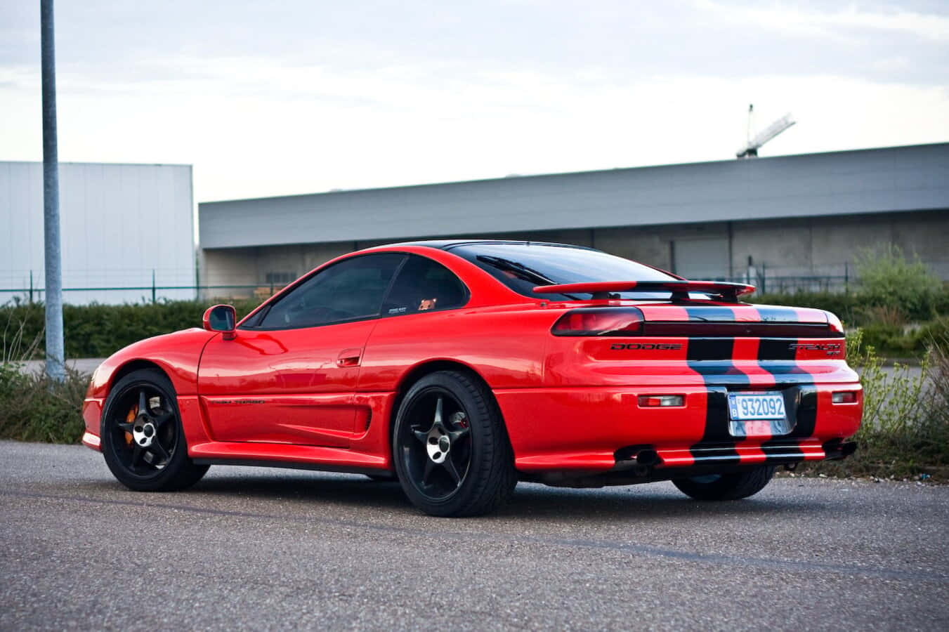 1991 Dodge Stealth 桌布 壁紙 — 一輛鮮紅色嘅Dodge Viper跑車，帶有黑色同藍色賽車條紋，停泊喺工業建築附近嘅瀝青路上。