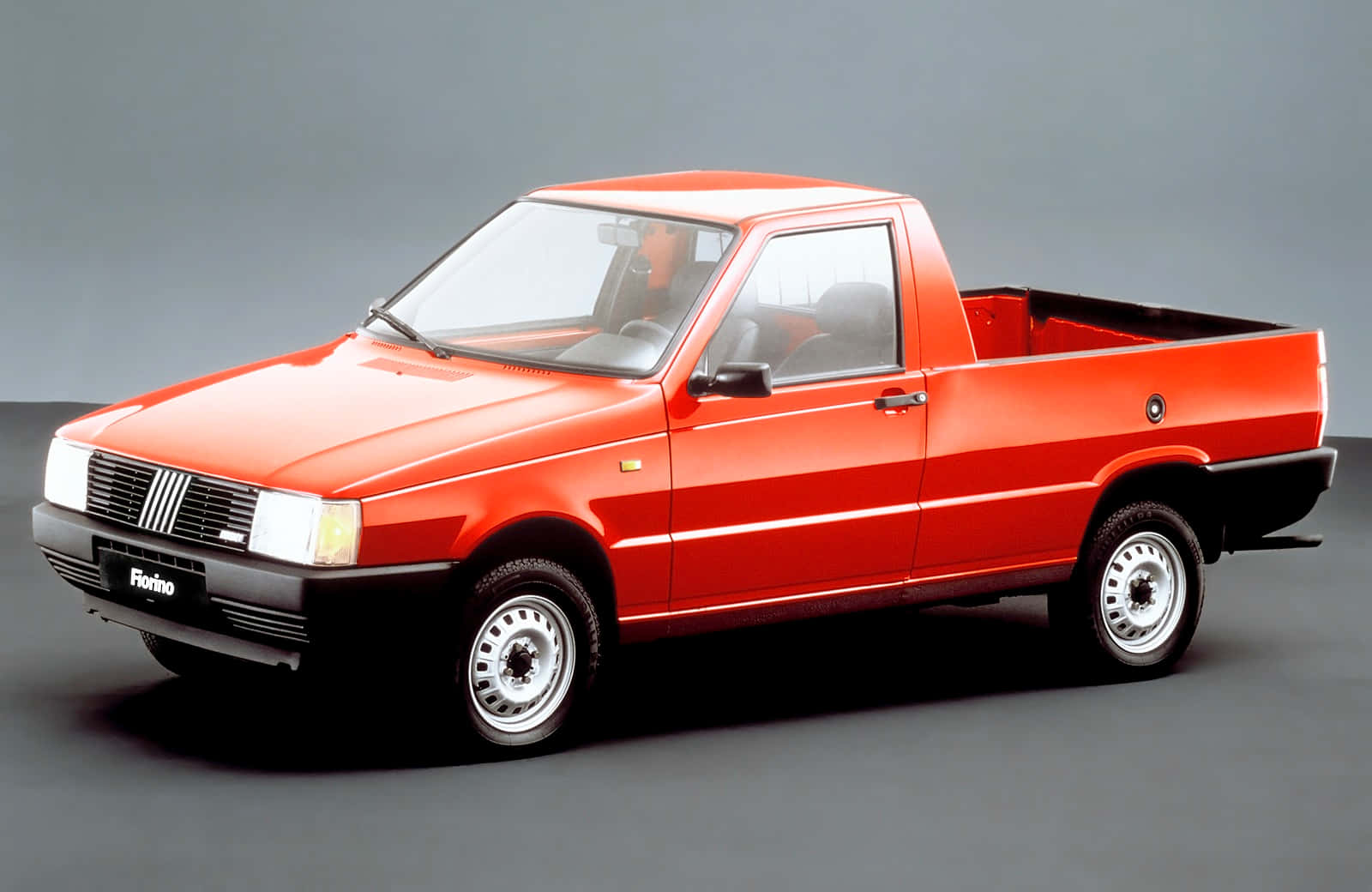 Fiat Fiorino 桌布 壁紙 — 一輛鮮紅色的菲亞特 Fiorino 皮卡車在灰色中性背景和柔和燈光的攝影棚中展示。