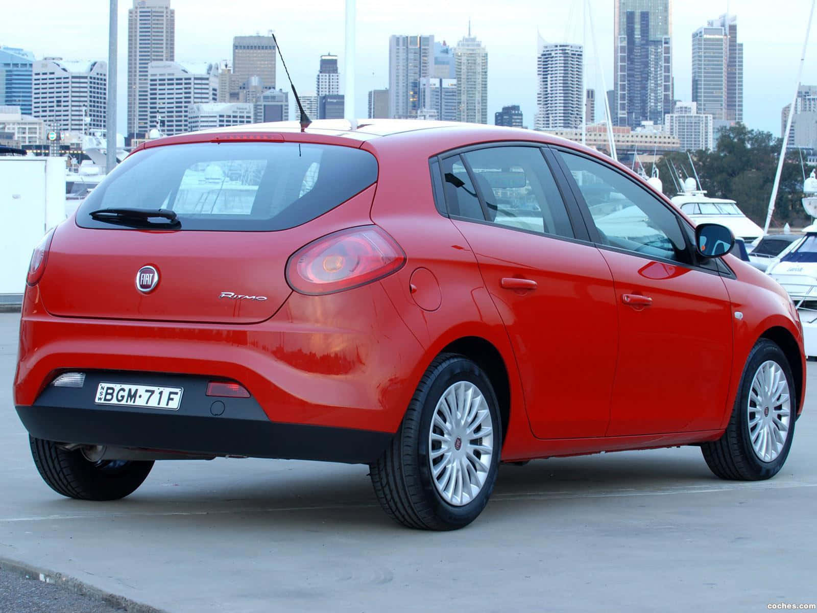 Fiat Ritmo 桌布 壁紙 — 一輛鮮紅色的快意Punto停泊在海濱，背景是城市天際線。