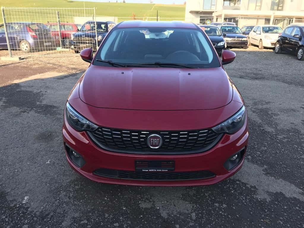 Fiat Tipo 桌布 壁紙 — 一輛鮮紅色的快意轎車在碎石停車場中向前，背景有其他車輛和圍欄。