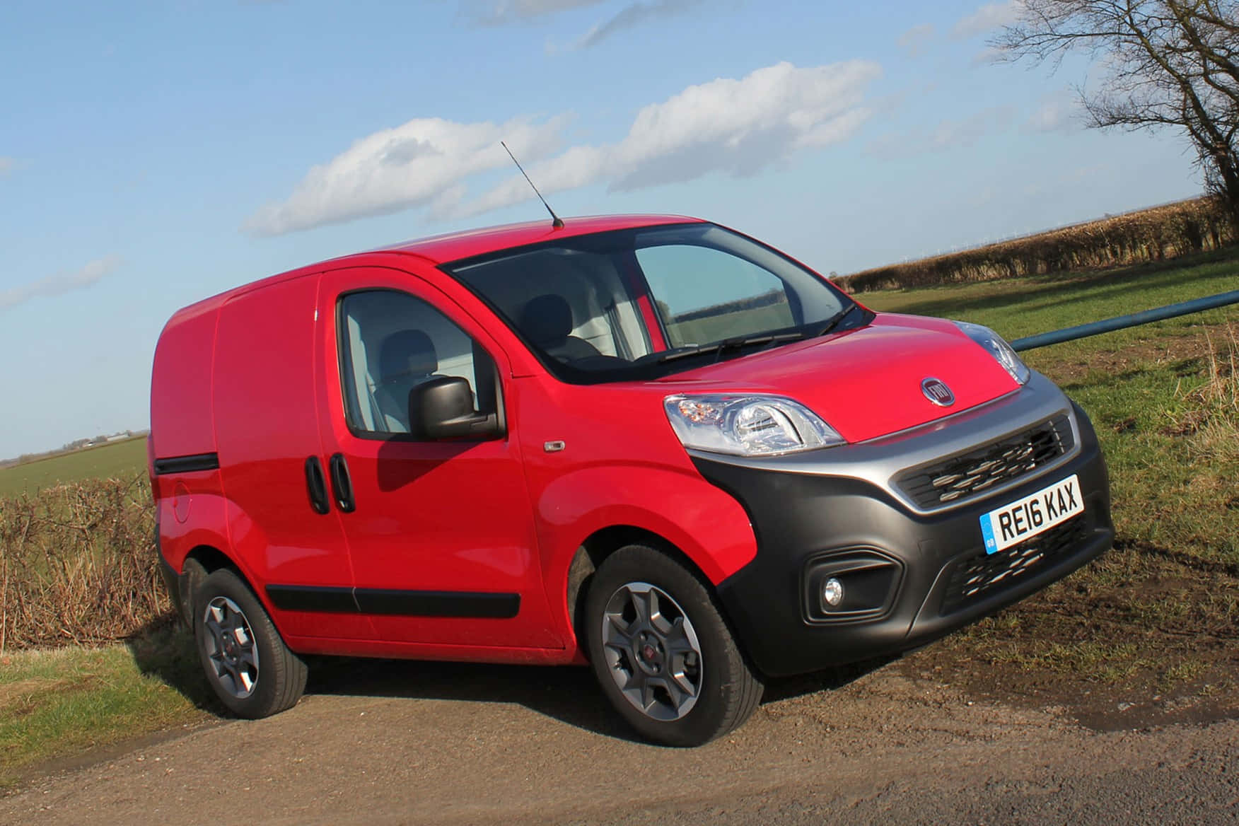 Fiat Fiorino 桌布 壁紙 — 一輛鮮紅色的Fiat客貨車停泊在碎石路上，旁邊是草地，天空局部多雲。
