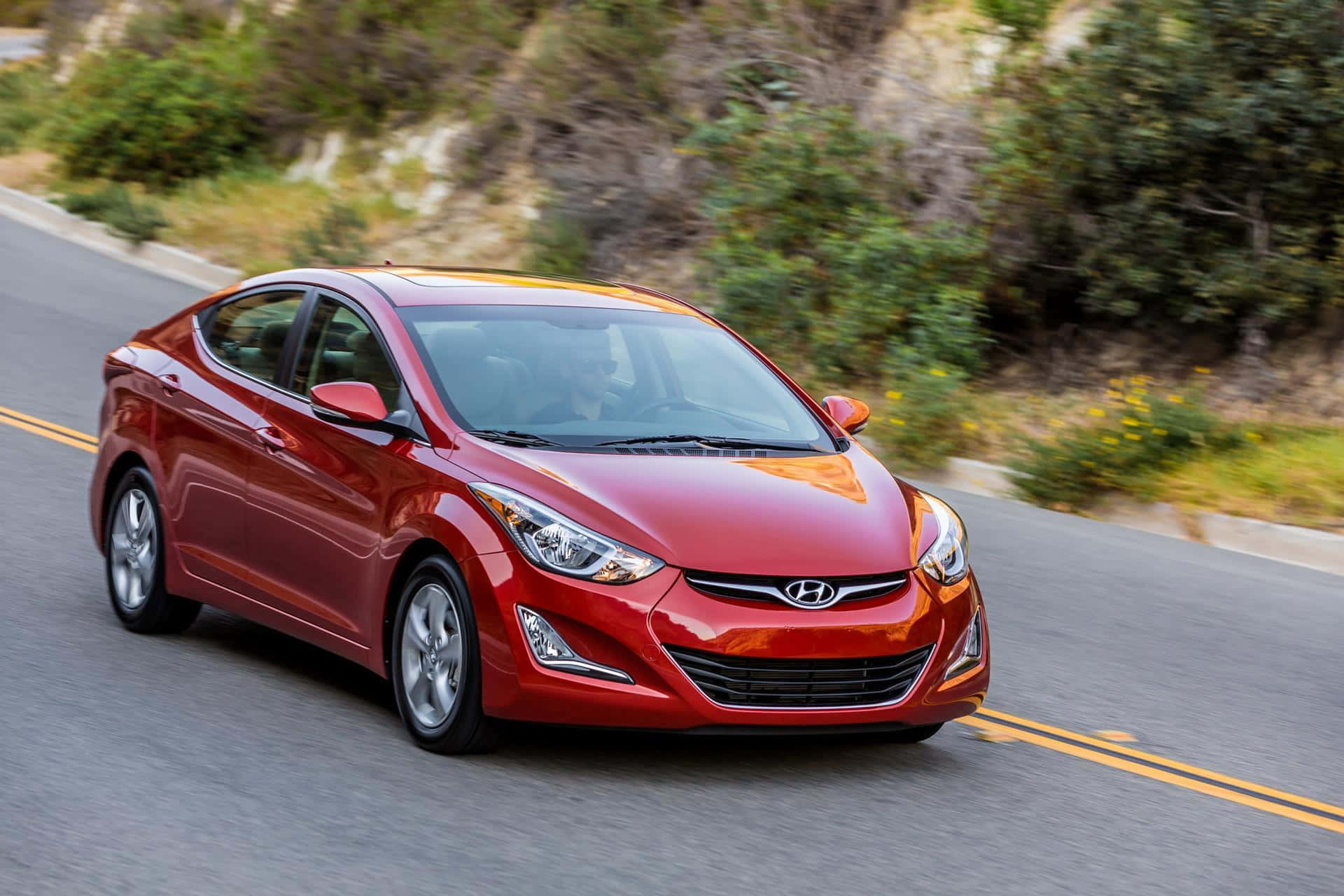Hyundai Elantra 桌布 壁紙 — 一輛鮮紅色的現代 Elantra 沿著蜿蜒的山路行駛，綠意隨著移動而模糊。
