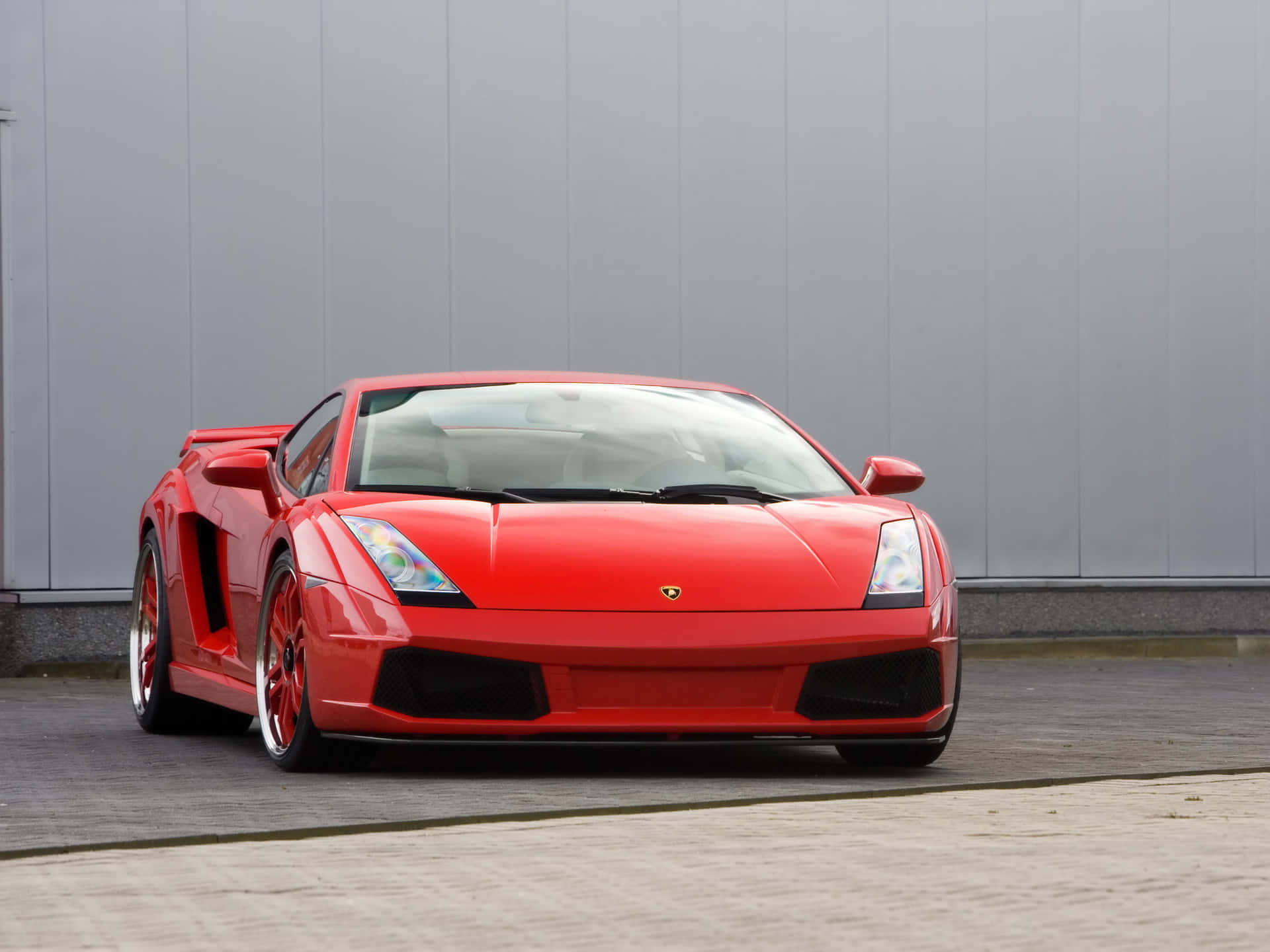 Lamborghini Gallardo 桌布 壁紙 — 一架鮮紅色林寶堅尼Gallardo跑車停泊在鋪砌路面上，背景是灰色工業牆。