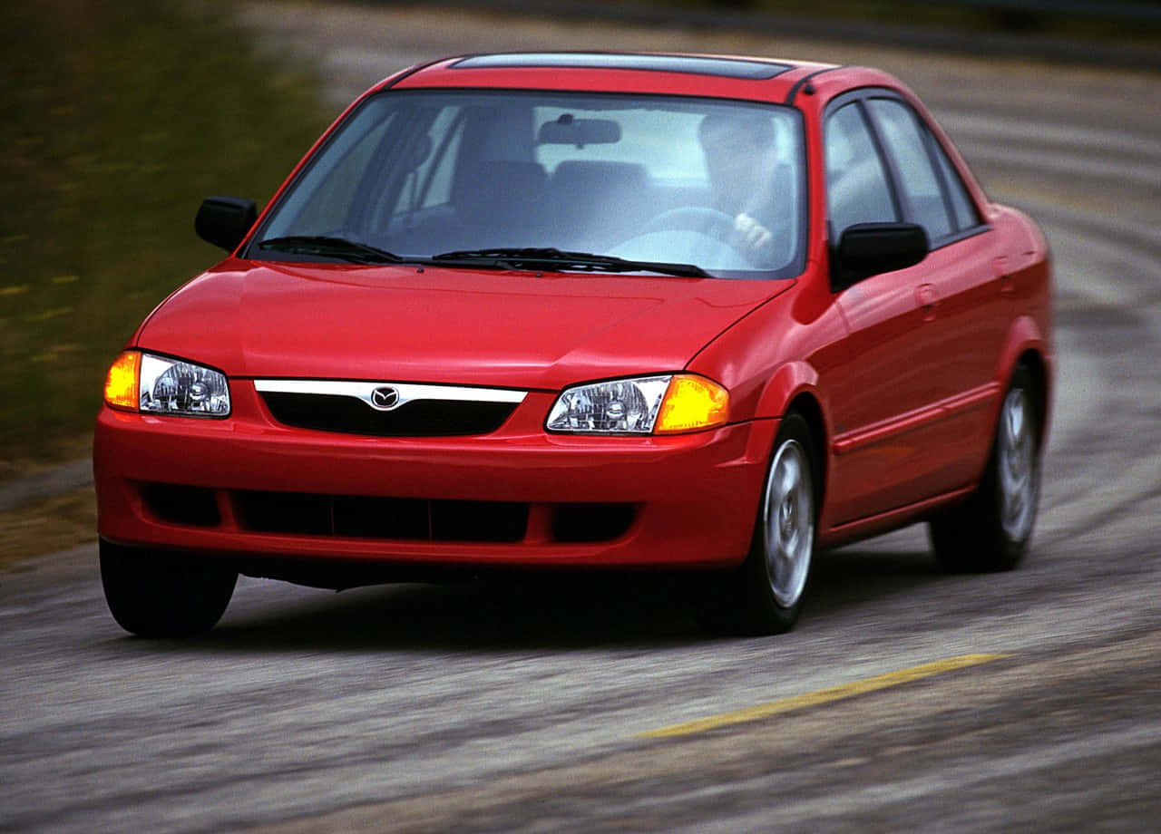 Mazda Protege 桌布 壁紙 — 一輛鮮紅色的萬事得房車在模糊的道路上疾馳，動態模糊強調了其動態移動。