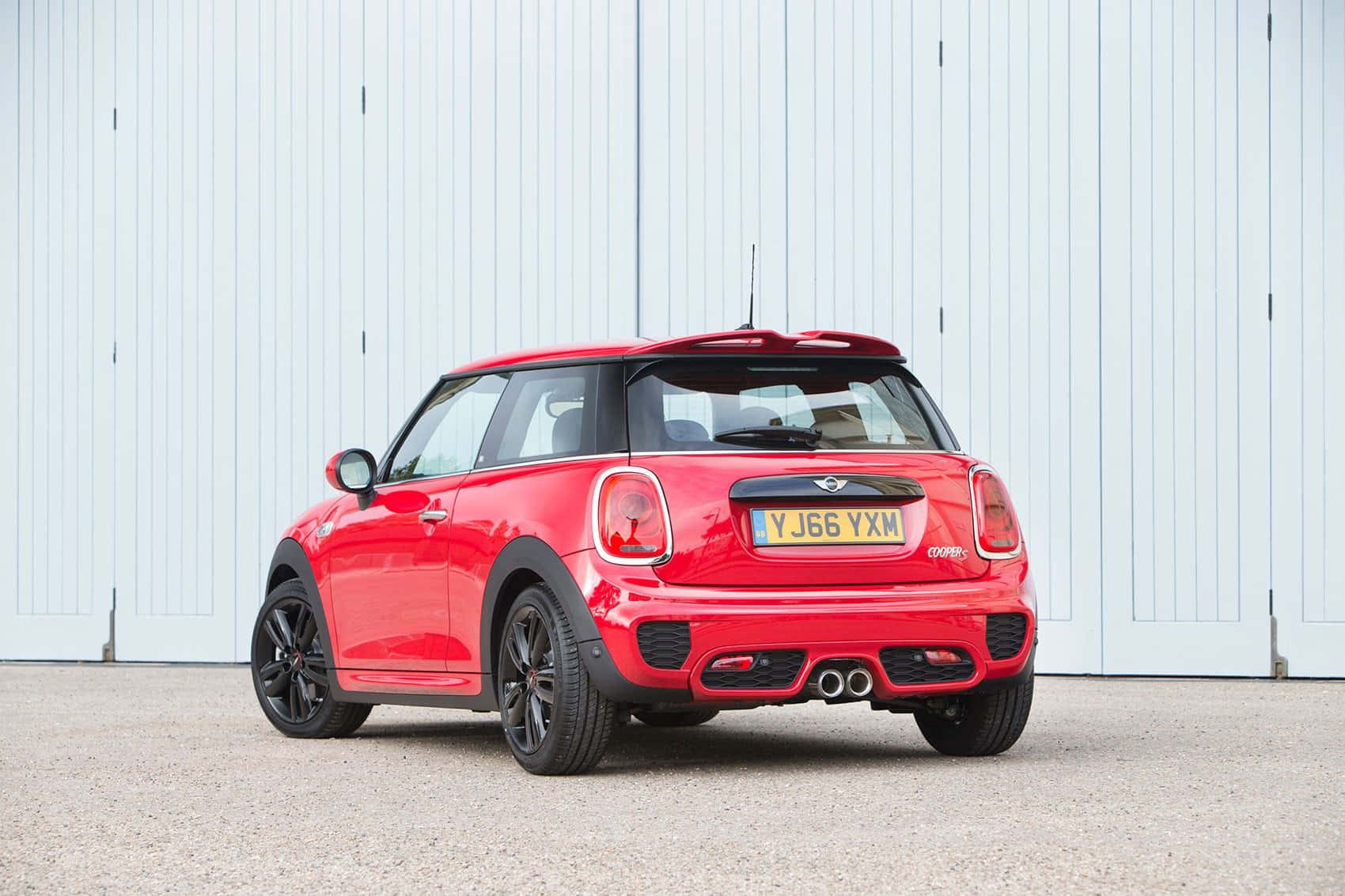 Mini Cooper S 桌布 壁紙 — 一輛鮮紅色的MINI Cooper S停放在白色工業門前，帶有黑色飾邊和雙排氣管。