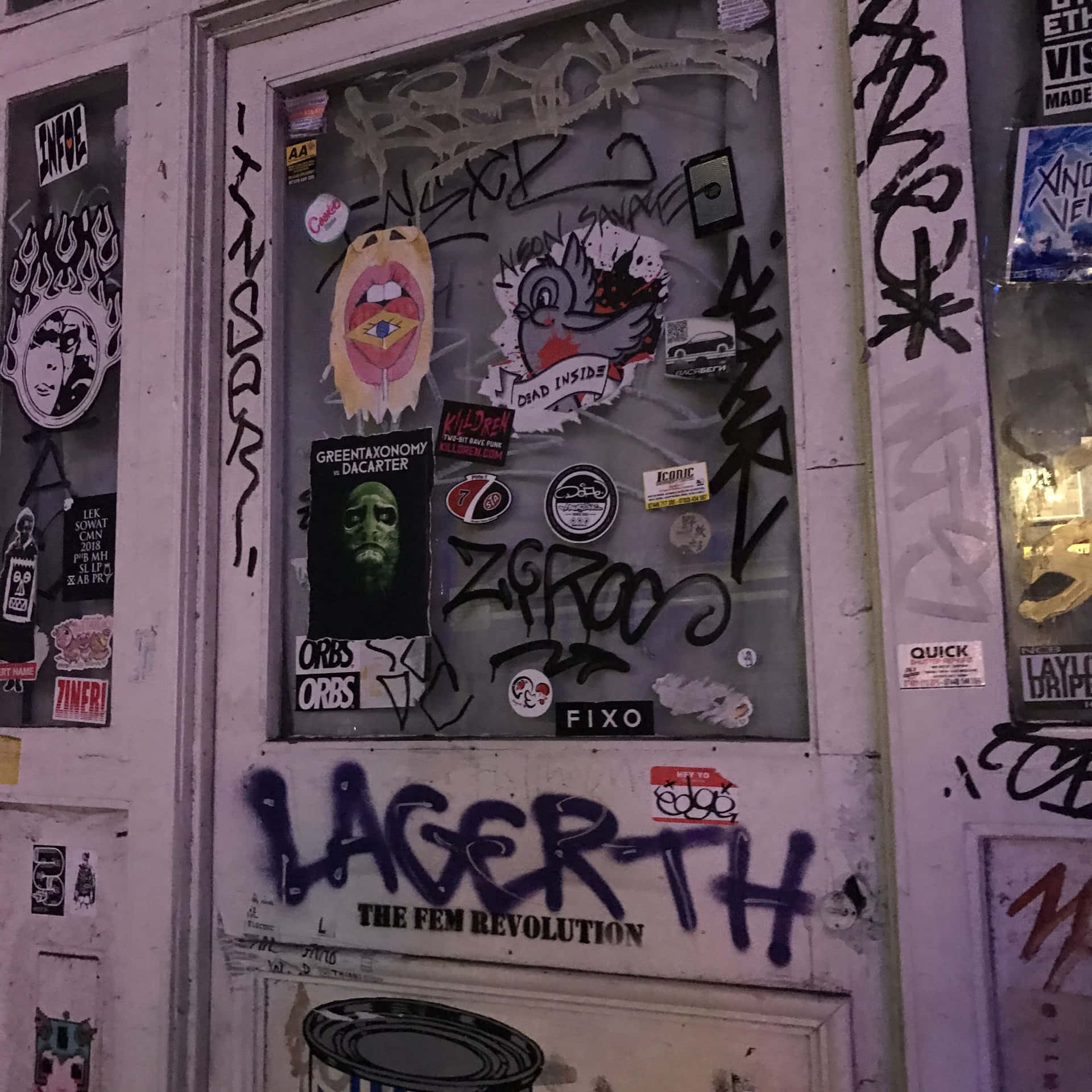 壁紙 — 一扇風化的門和牆壁，在昏暗的夜間燈光下覆蓋著多層塗鴉貼紙和標籤。