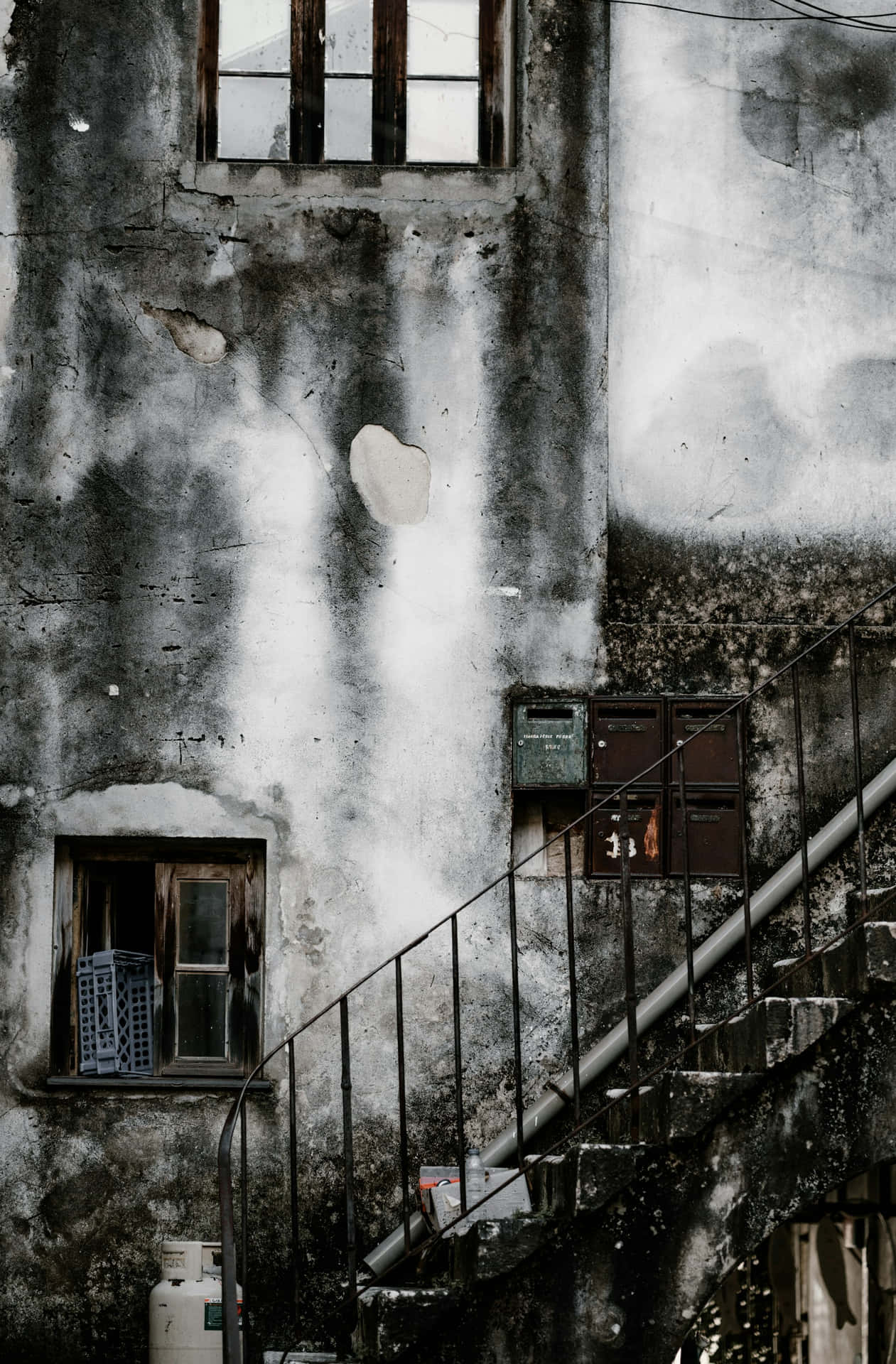  壁紙 — 一座歷經風霜的都市建築，白色油漆剝落，生鏽的金屬樓梯蜿蜒而上，攀附在日漸腐朽的外牆上。