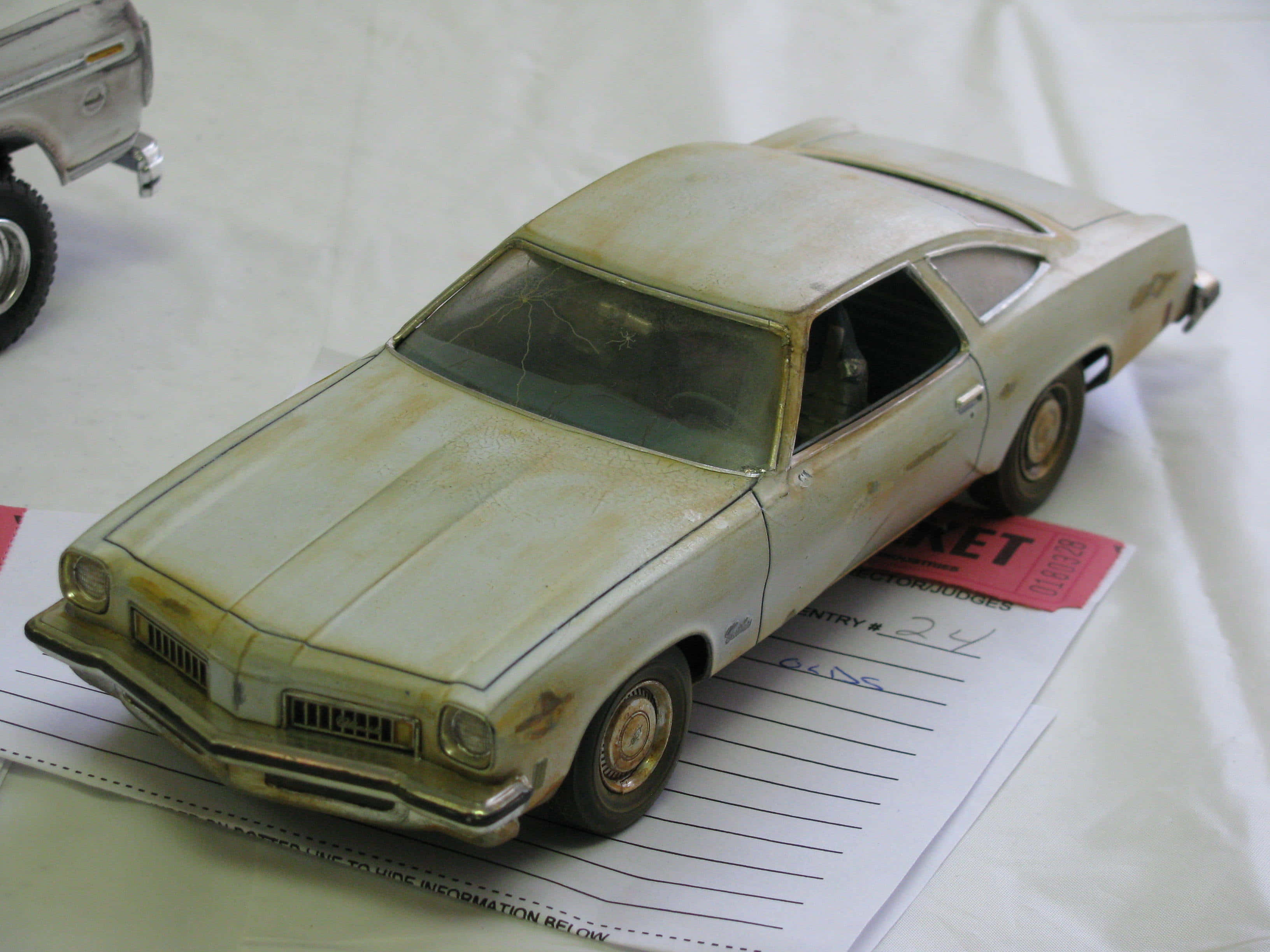 Car Model 桌布 壁紙 — 一個風化的復古汽車模型，帶有鐵鏽和污垢，放在白色背景的紙質報名表上。