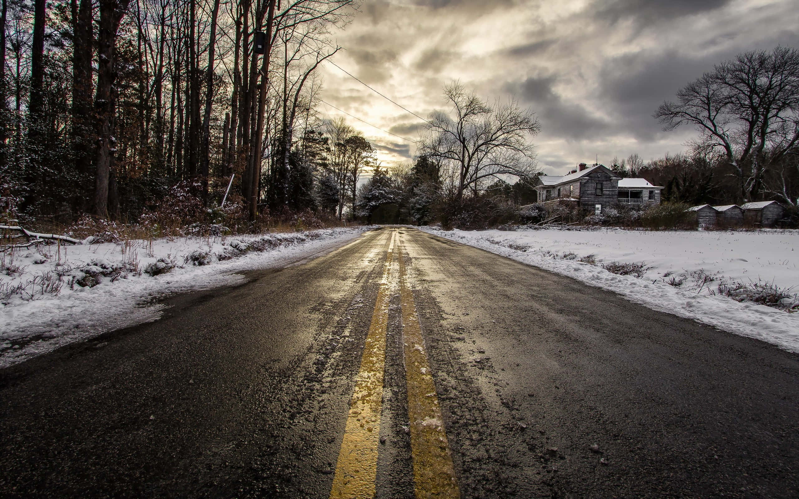Snowy Road 桌布 壁紙 — 一條濕漉漉的冬季道路，黃色標線延伸至陰天下的一座孤獨房屋。
