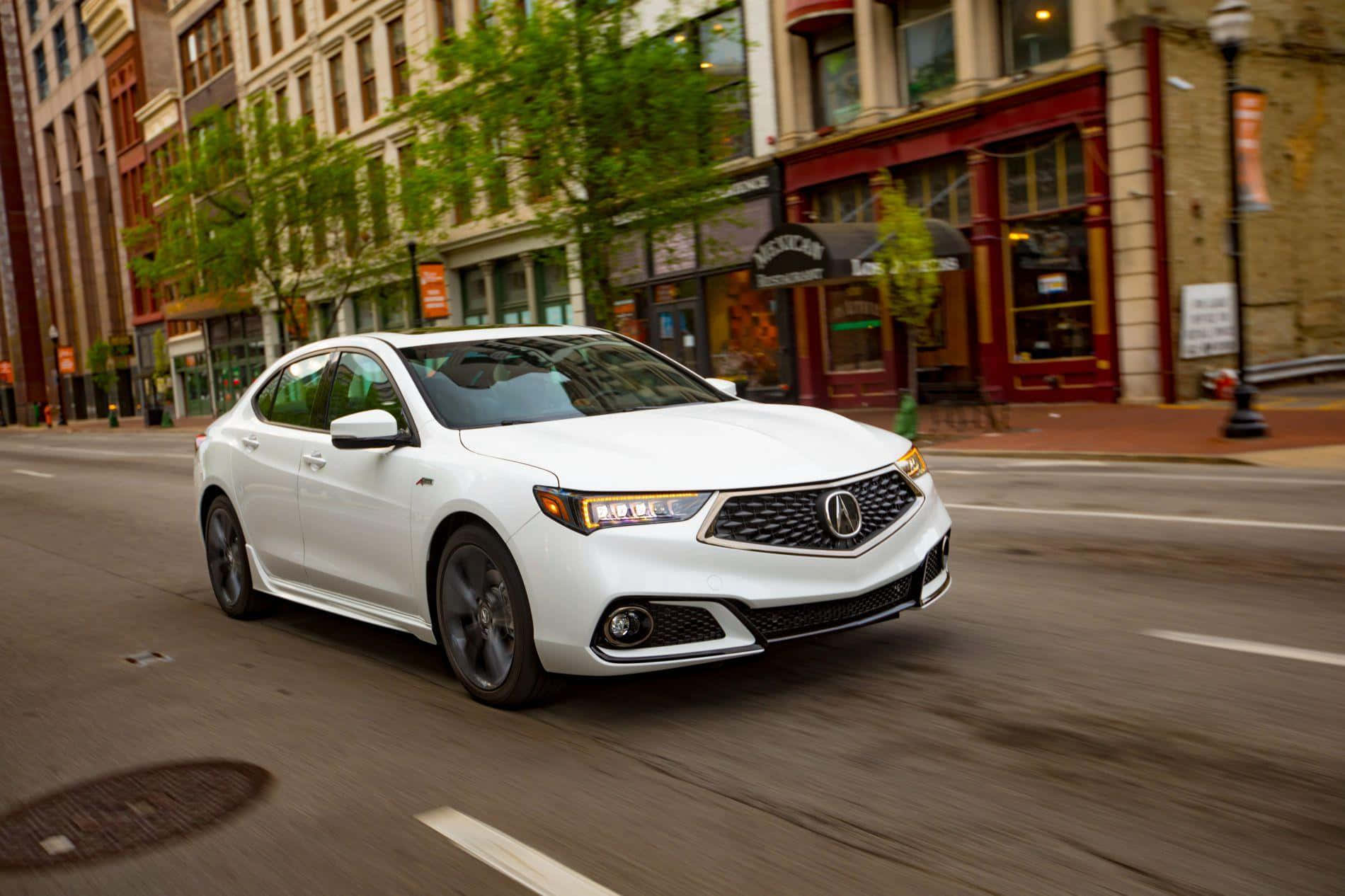 Acura Tlx 桌布 壁紙 — 一輛白色Acura轎車在兩旁種滿樹木的城市街道上飛馳，背景有模糊的動態和商店門面。