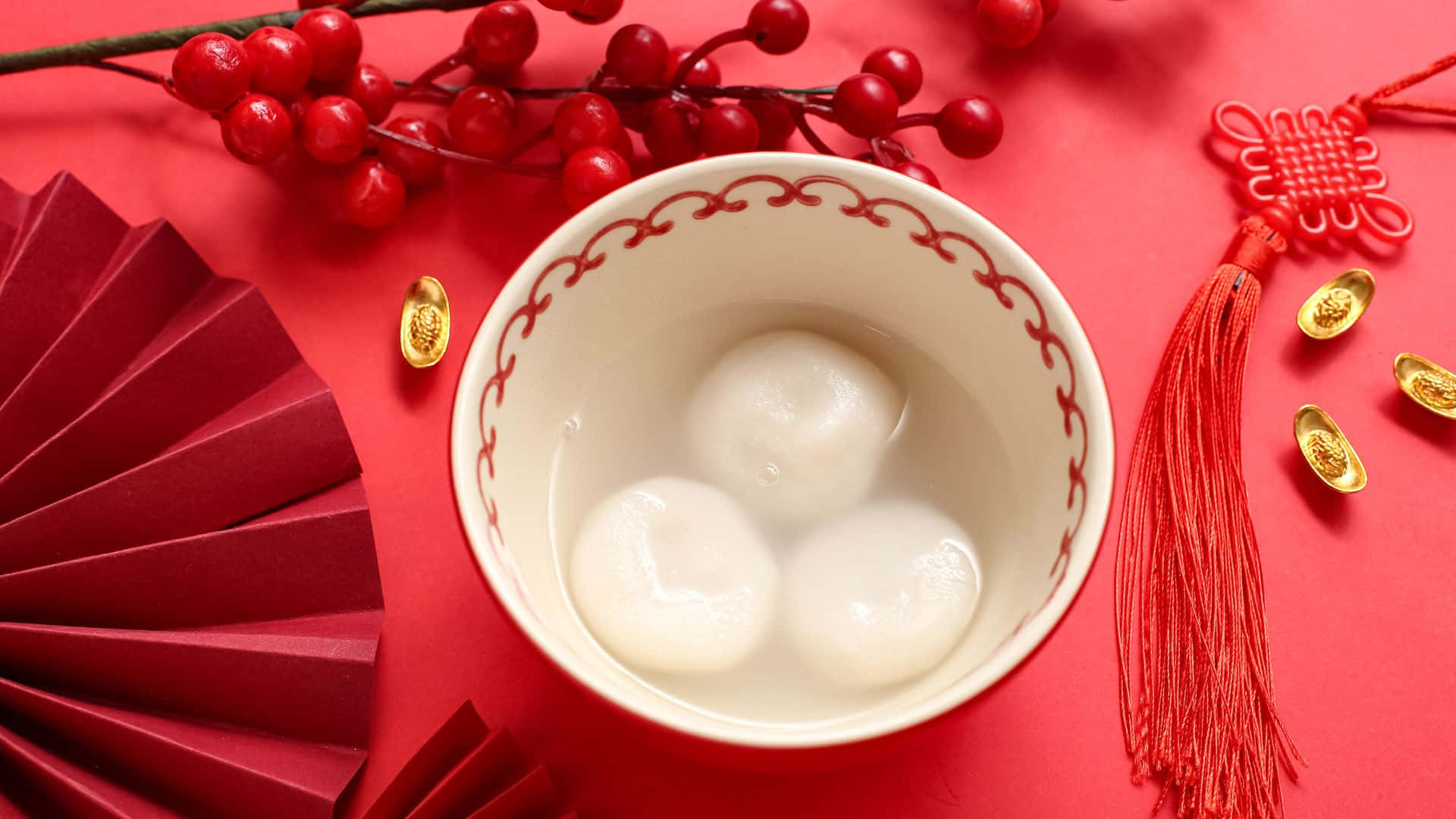  壁紙 — 一個白色碗盛著三個糯米湯圓在清湯中，背景是鮮紅色，點綴著喜慶的中國新年裝飾。