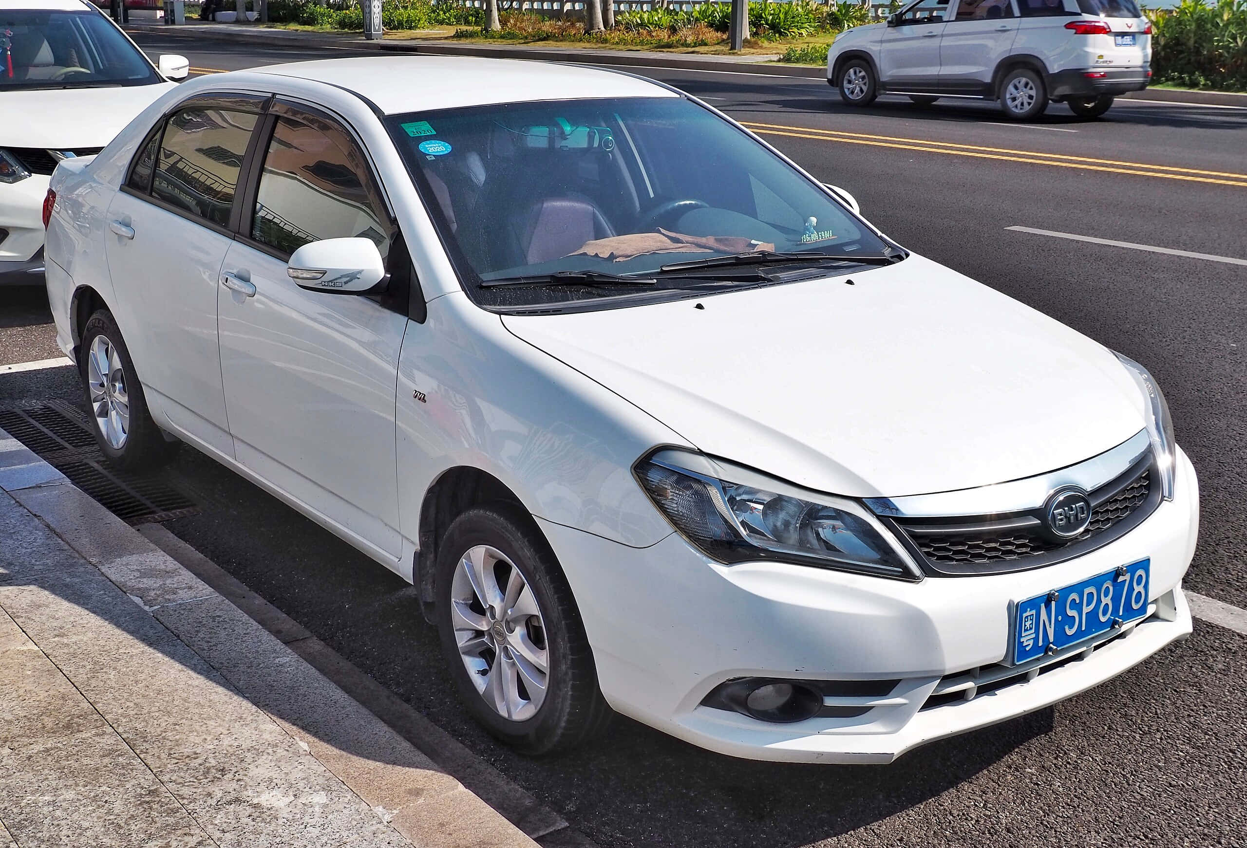 Byd F3 桌布 壁紙 — 一輛白色比亞迪轎車停泊在陽光明媚的街道上，背景有其他汽車和綠化。