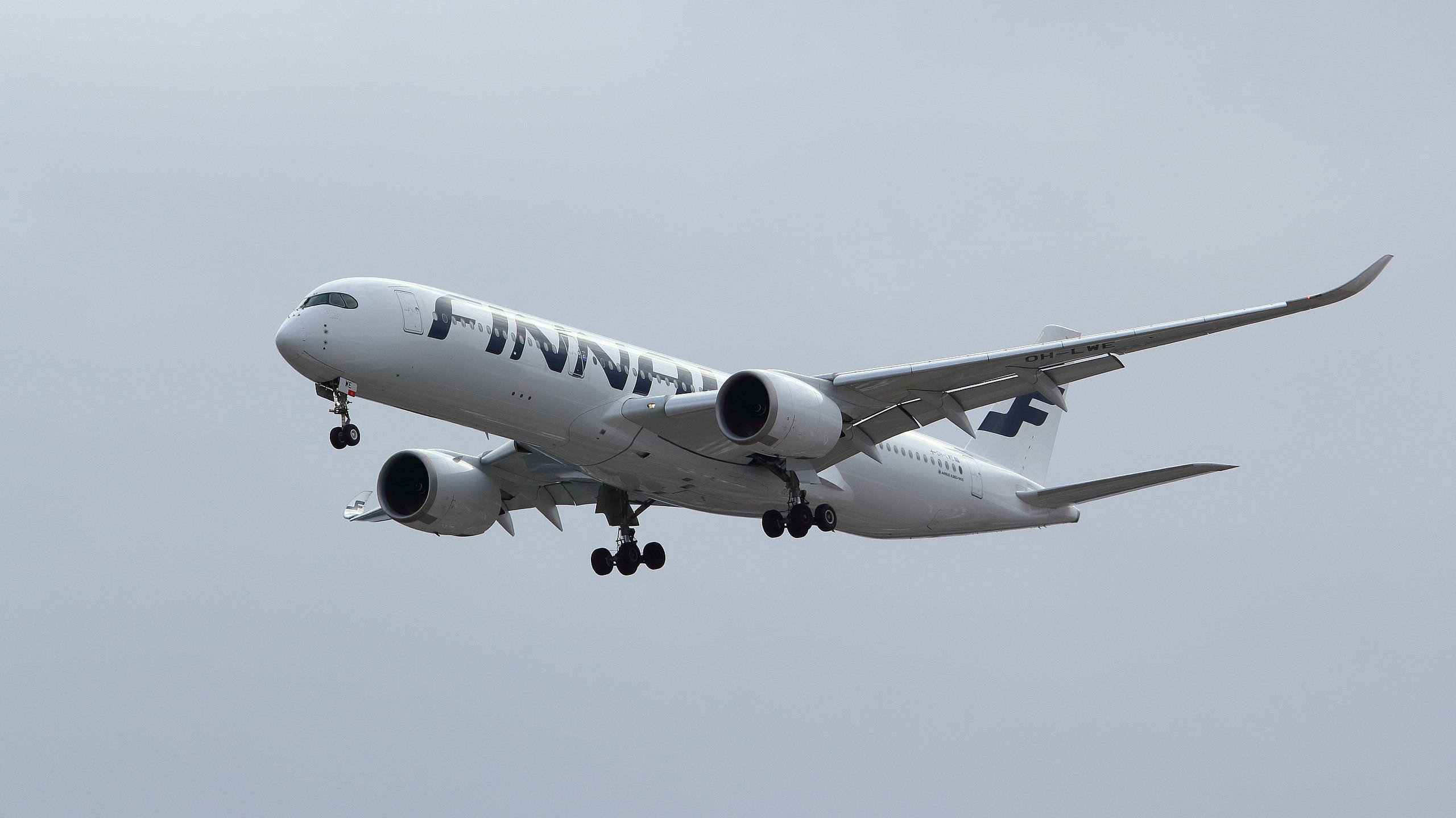 芬蘭航空領先邊緣飛機 壁紙 — 一架白色芬蘭航空空中巴士A350放下起落架，在暗淡的灰色天空中翱翔。