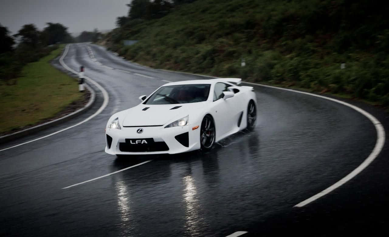 Lexus Lfa 桌布 壁紙 — 一輛白色Lexus LFA跑車在陰天時穿過茂密綠色森林中的潮濕蜿蜒道路。