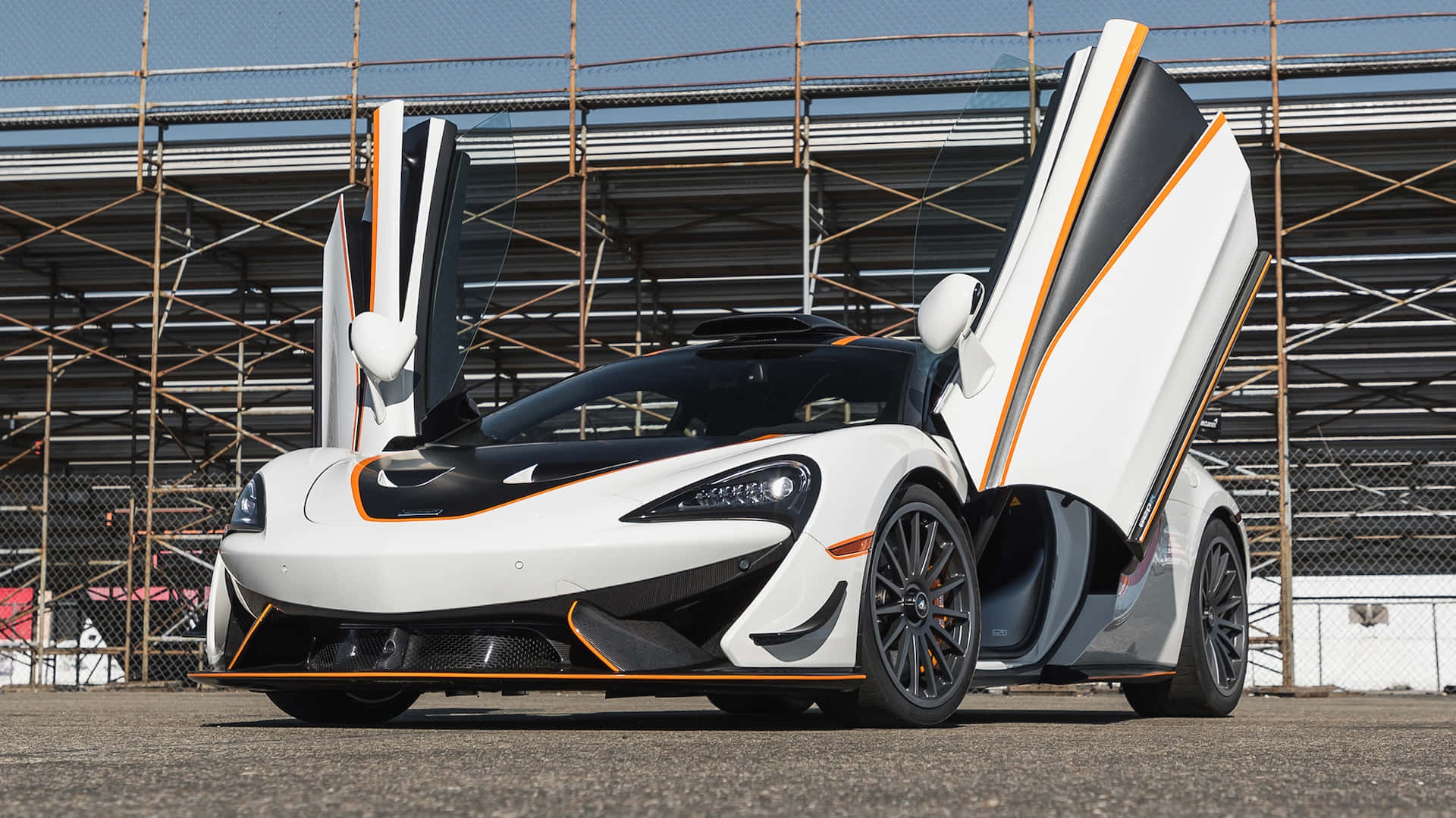 Mclaren 620r 桌布 壁紙 — 一輛帶有橙色點綴和打開蝴蝶門的白色McLaren跑車停在賽道上。