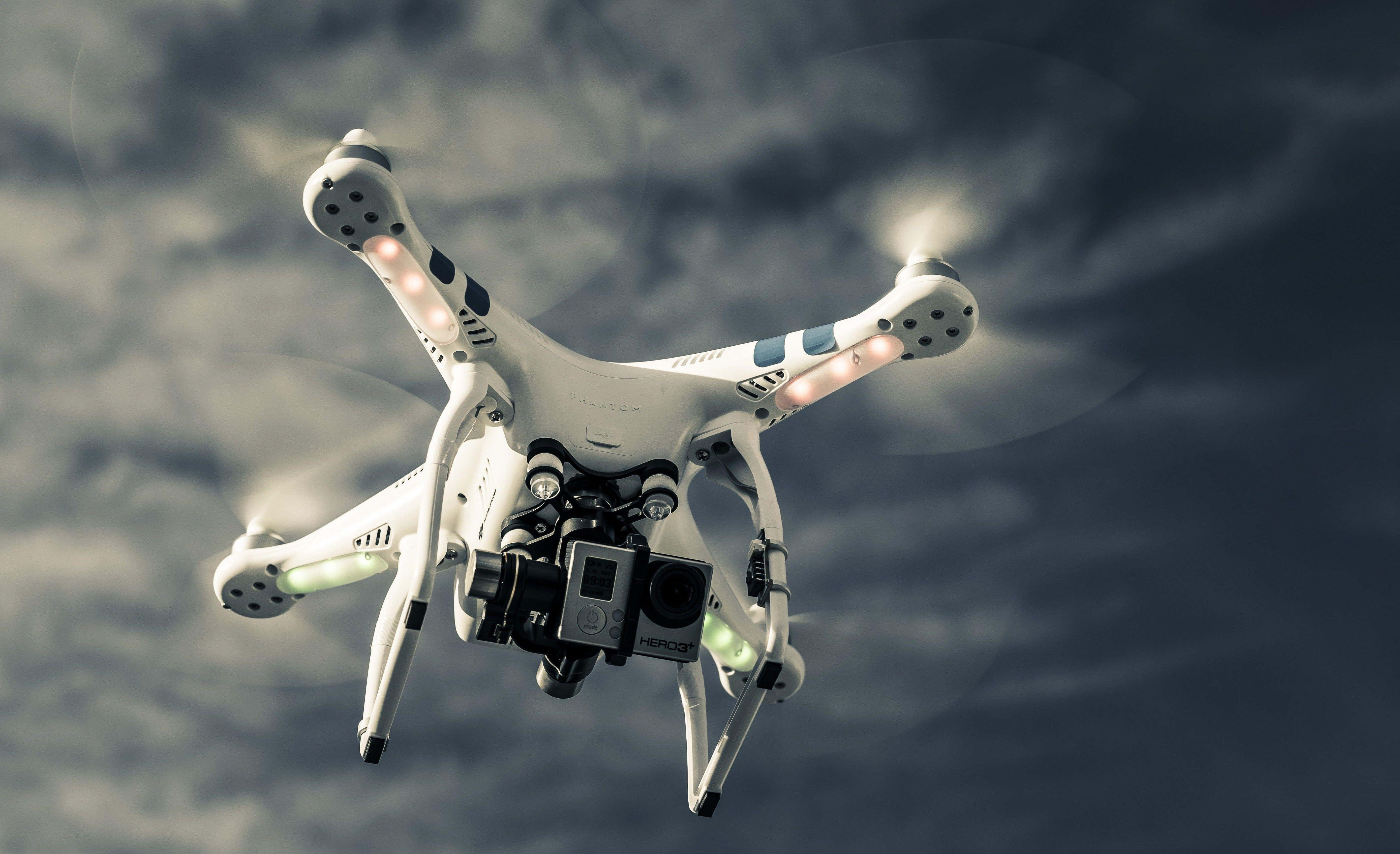 Drone Camera 桌布 壁紙 — 一架白色四軸無人機帶有發光螺旋槳，在戲劇性的多雲天空中盤旋。