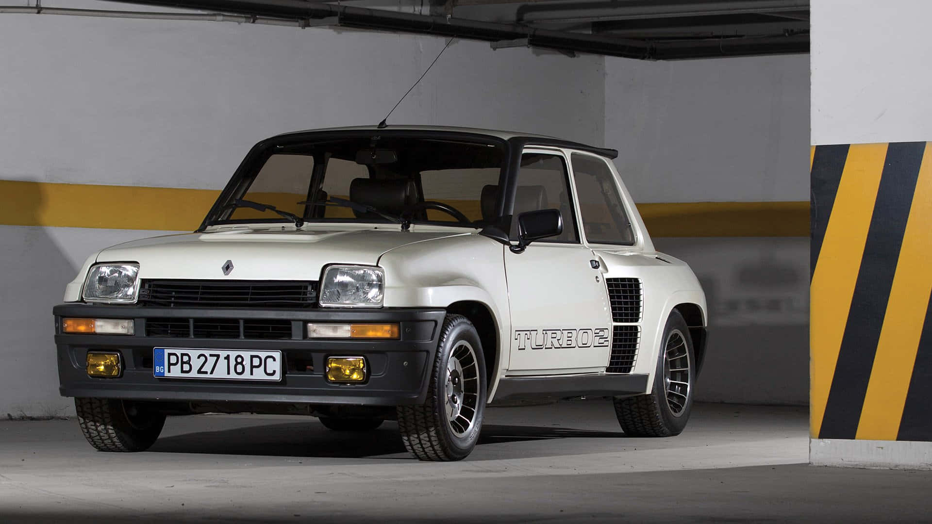 Renault 5 Turbo 桌布 壁紙 — 一輛白色雷諾5 Turbo 2跑車停放在有黃色條紋柱子的混凝土地下停車場。