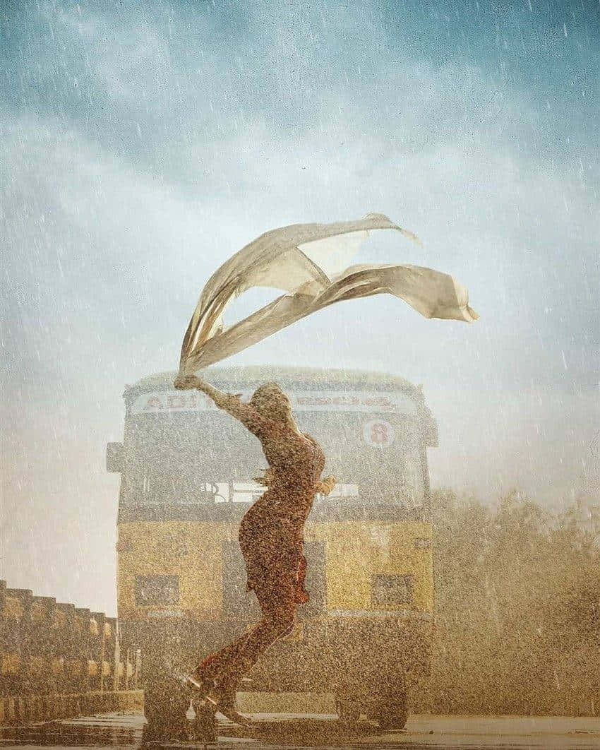  壁紙 — 一名女子在傾盆大雨中，圍巾飄揚，以黃色巴士為背景，在粗糙的城市環境中跳舞。