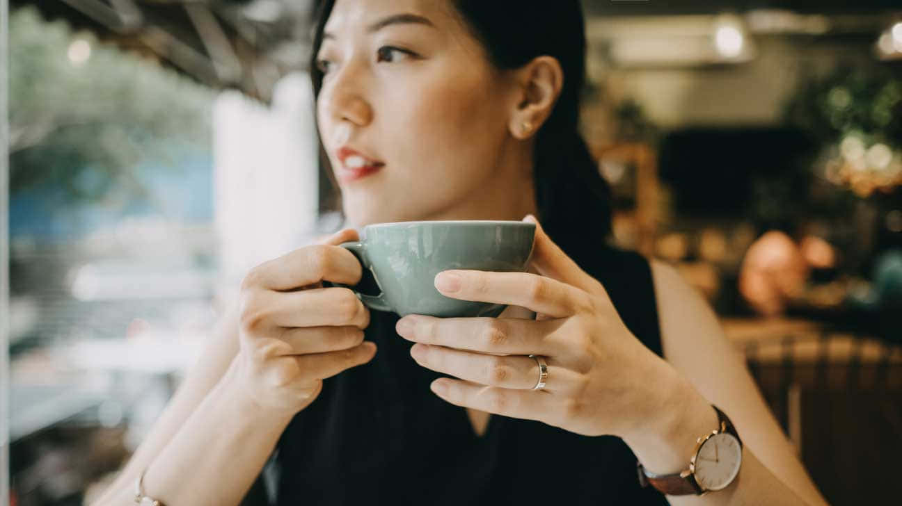  壁紙 — 一位女士在咖啡館裡拿著一個綠色杯子，若有所思地凝視窗外。