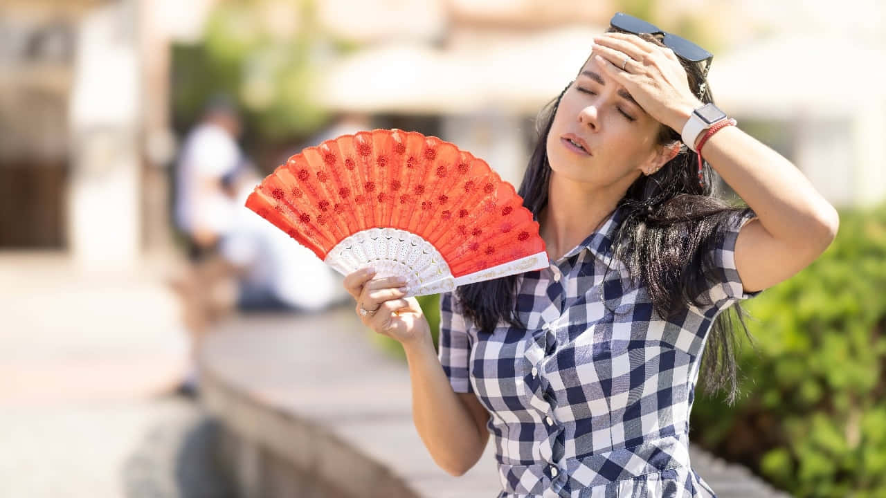  壁紙 — 一位身穿格仔裙嘅女士用紅色扇撥涼，同時遮擋住塊面免受猛烈陽光照射。