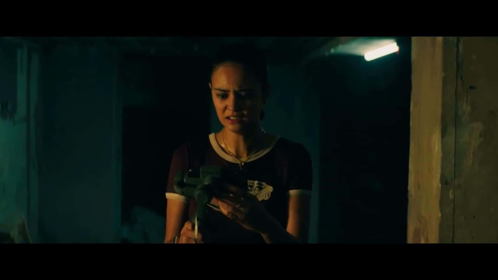 Courtney Eaton 桌布 壁紙 — 一個女人在燈光昏暗的房間裡，在單一頭頂燈光下，表情緊張地拿著一把槍。