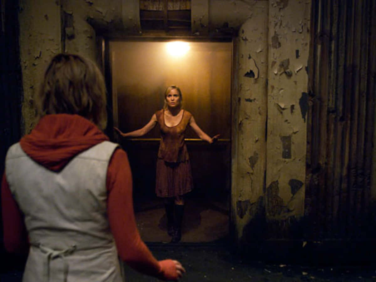 Silent Hill Characters 桌布 壁紙 — 一個穿著骯髒裙子的女人站在光線昏暗的電梯門口，面對另一個穿著紅色連帽衫的人。