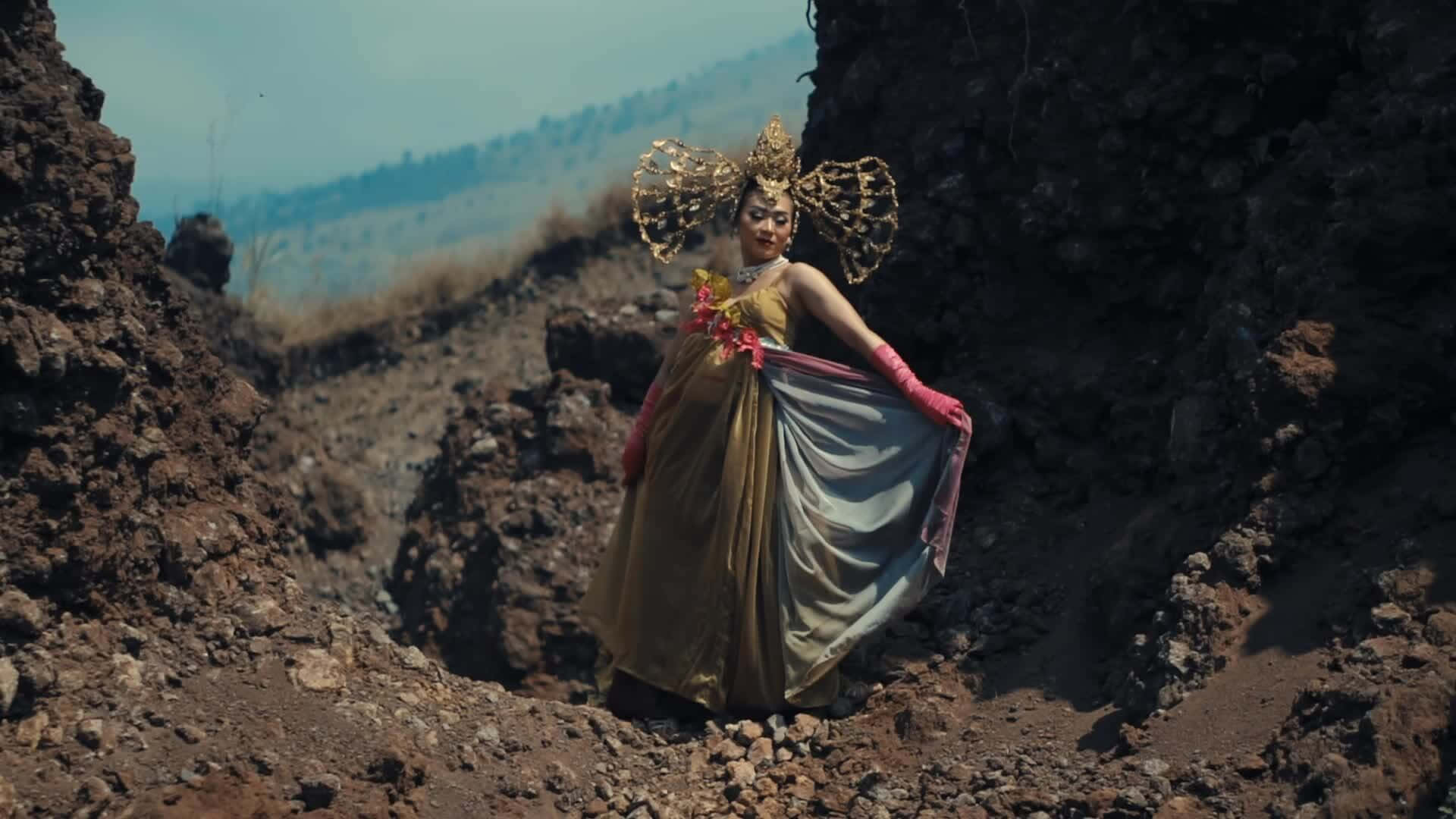 一位身穿金色長袍和華麗頭飾的女性，站在火山景觀中。 — 唯美蝴蝶動圖 壁紙