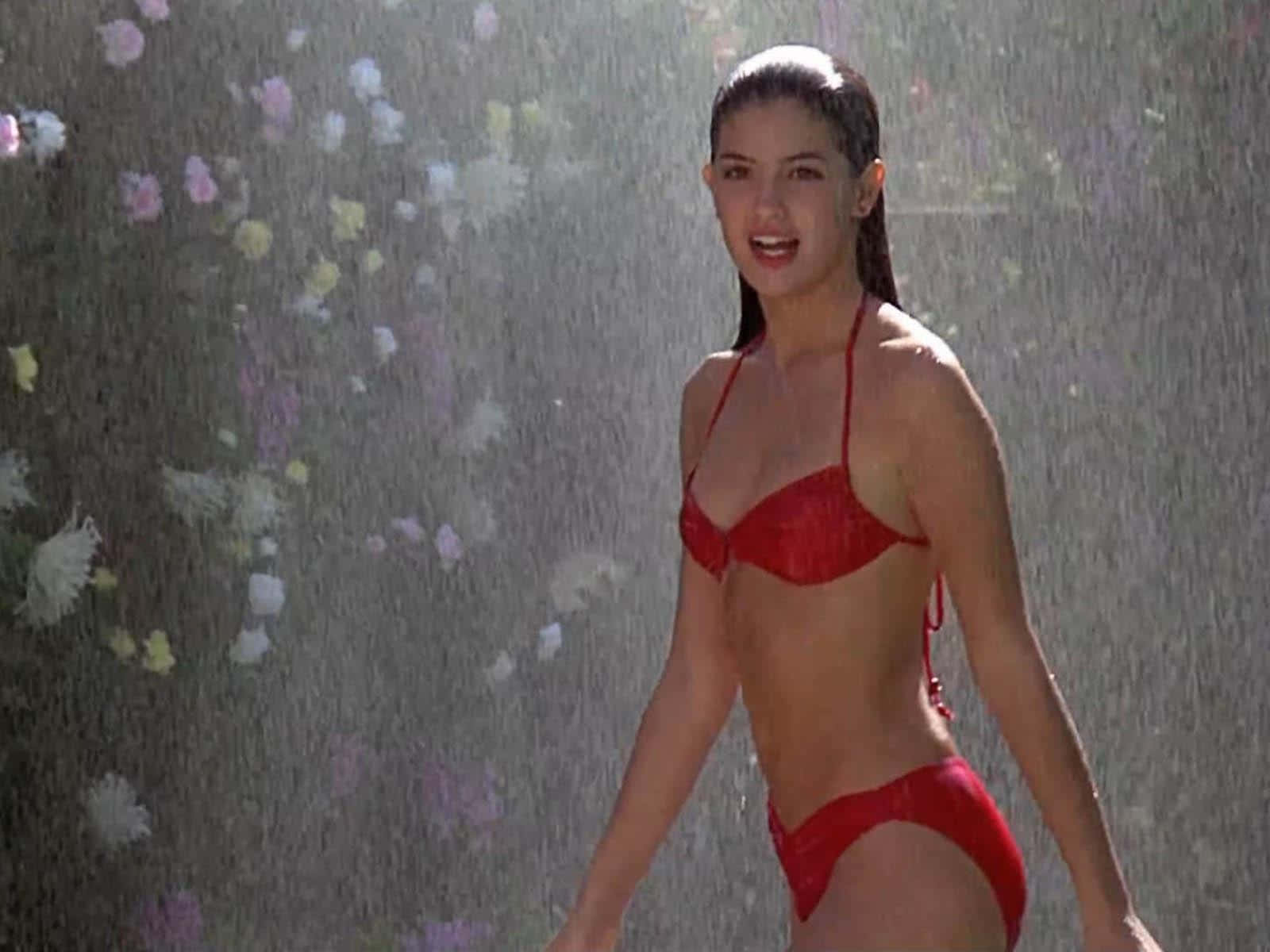 Phoebe Cates 桌布 壁紙 — 一位身穿紅色比基尼的女性在雨中微笑，背景有模糊的彩色花朵。