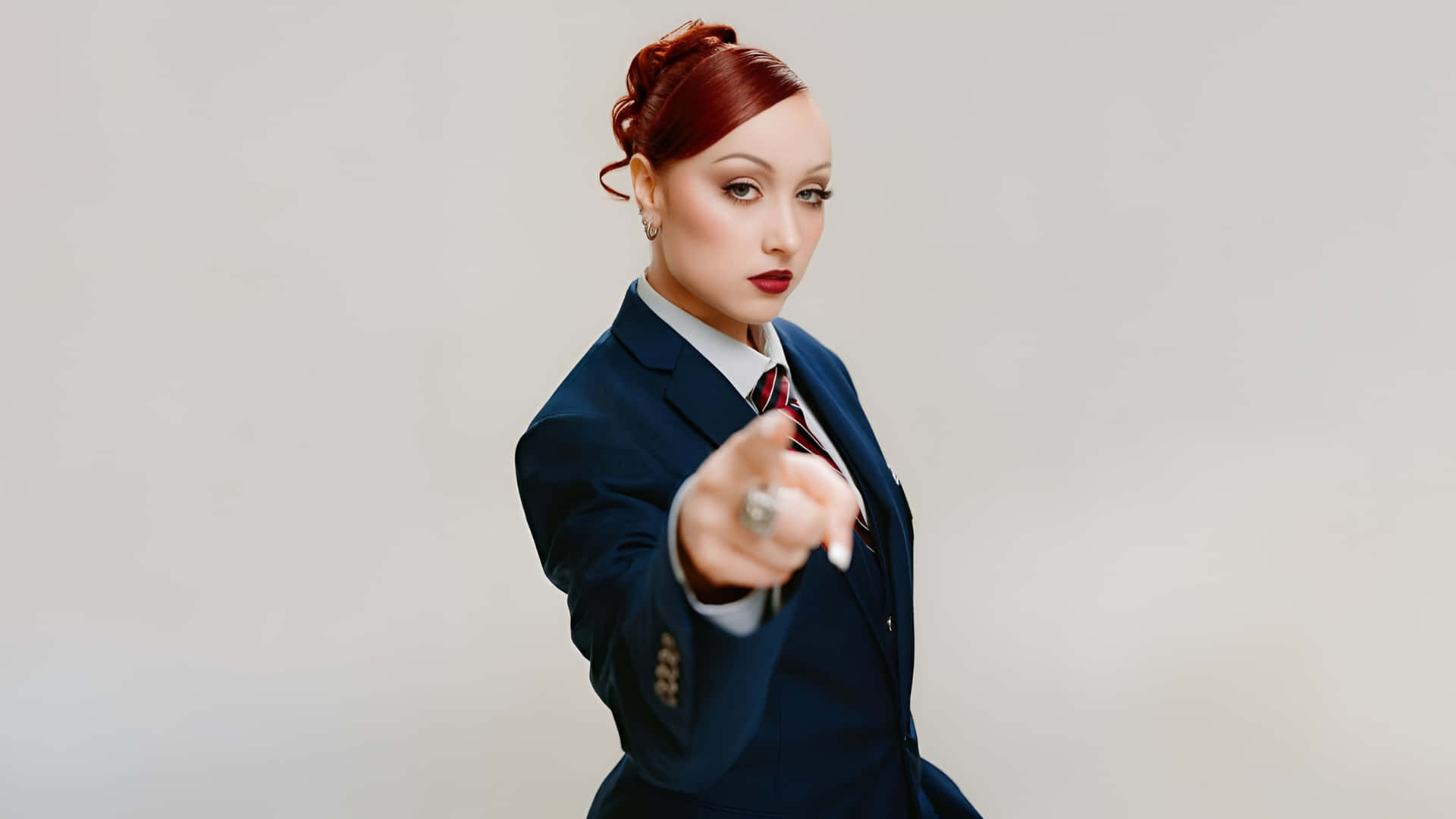  壁紙 — 一位身穿利落海軍藍西裝的女性，在純色背景下以自信的眼神直接指向觀看者。