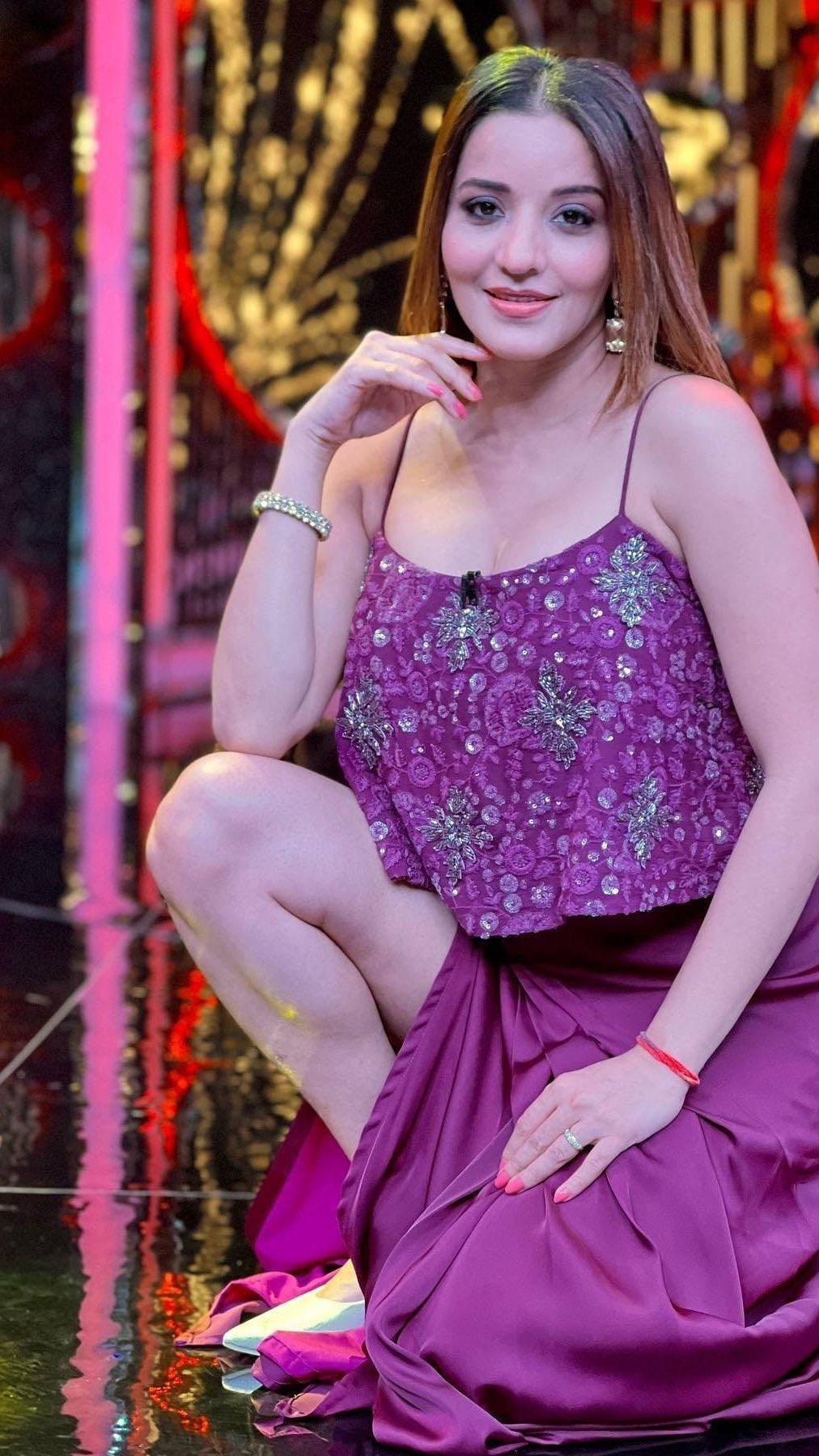 身穿紫色連衣裙的女性在帶有反射地板的燈光舞台上擺姿勢。