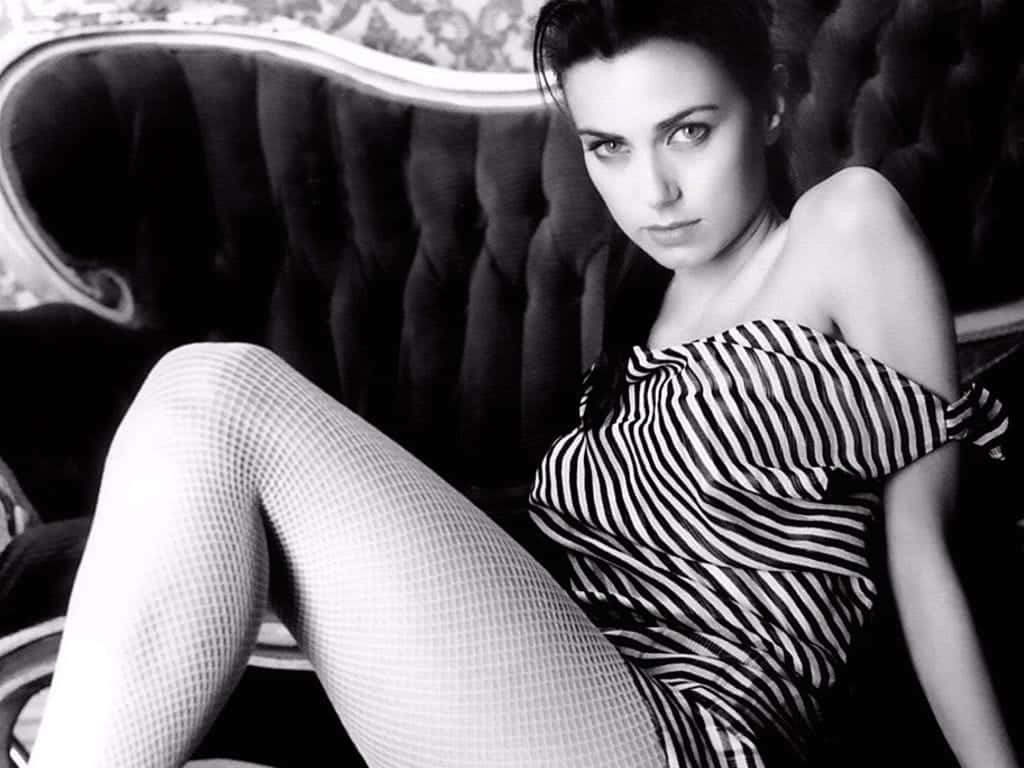Mia Kirshner 桌布 壁紙 — 一位穿著條紋露肩連衣裙和漁網襪的女性在一張華麗的簇絨沙發上以黑白照片誘人地擺姿勢。