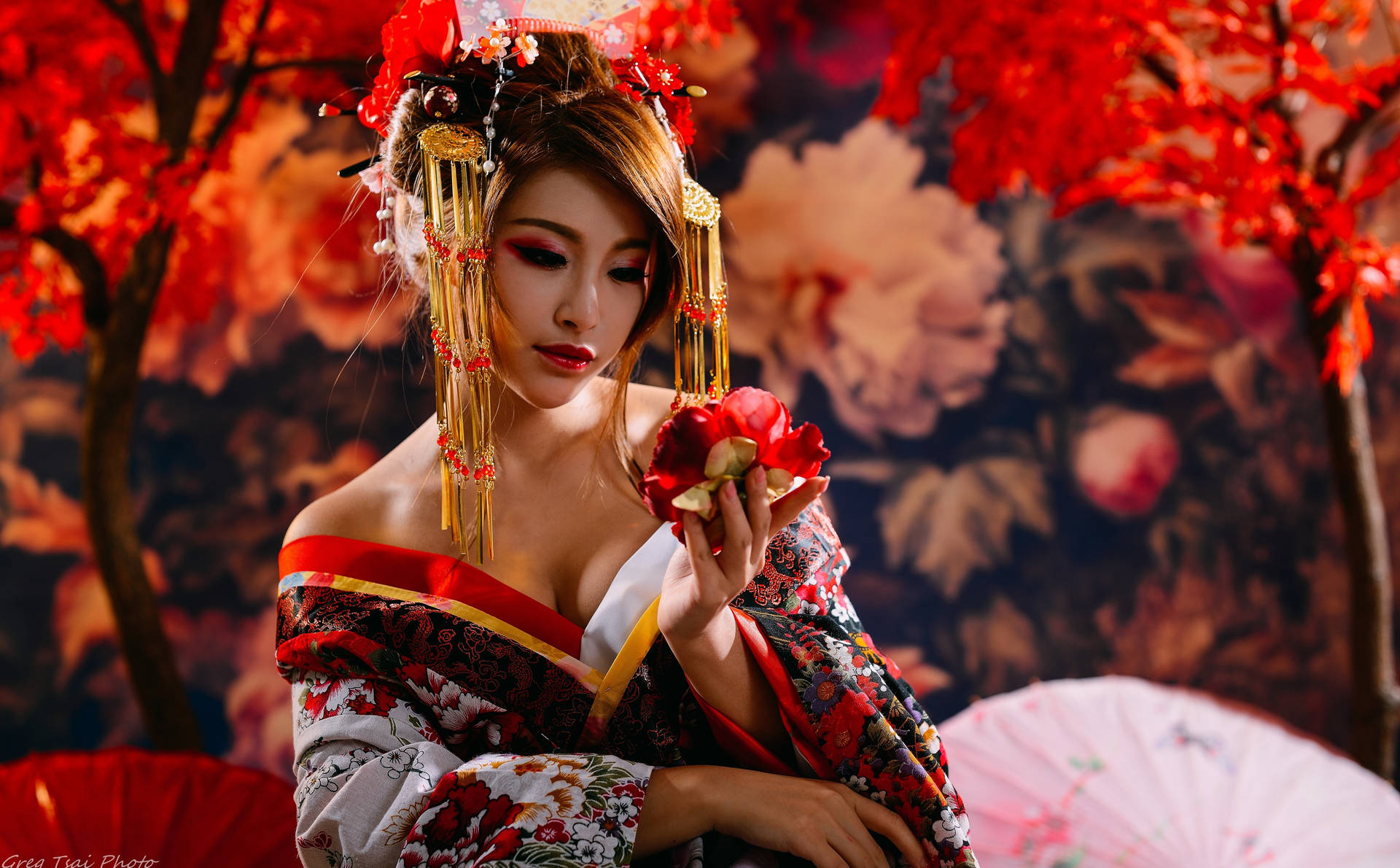 一位身穿傳統和服的藝妓，在秋樹下持著一朵紅花。