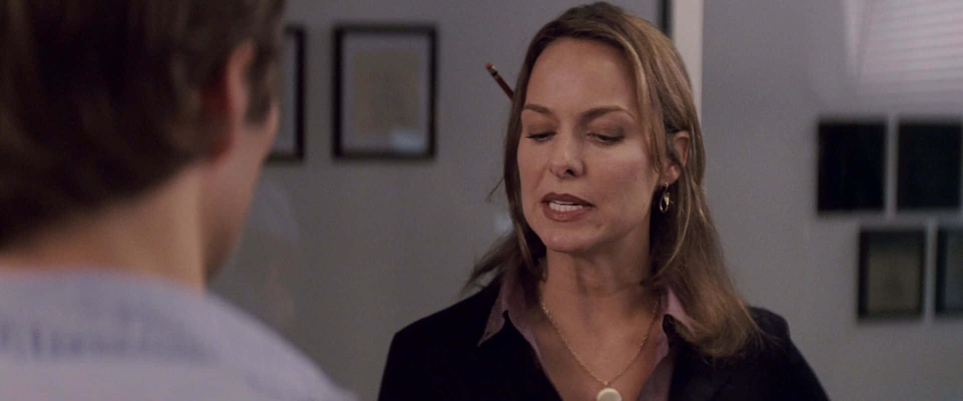 Melora Hardin 桌布 壁紙 — 一位耳後夾著鉛筆的女性在柔和光線的室內辦公室環境中專注地與一名男性交談。