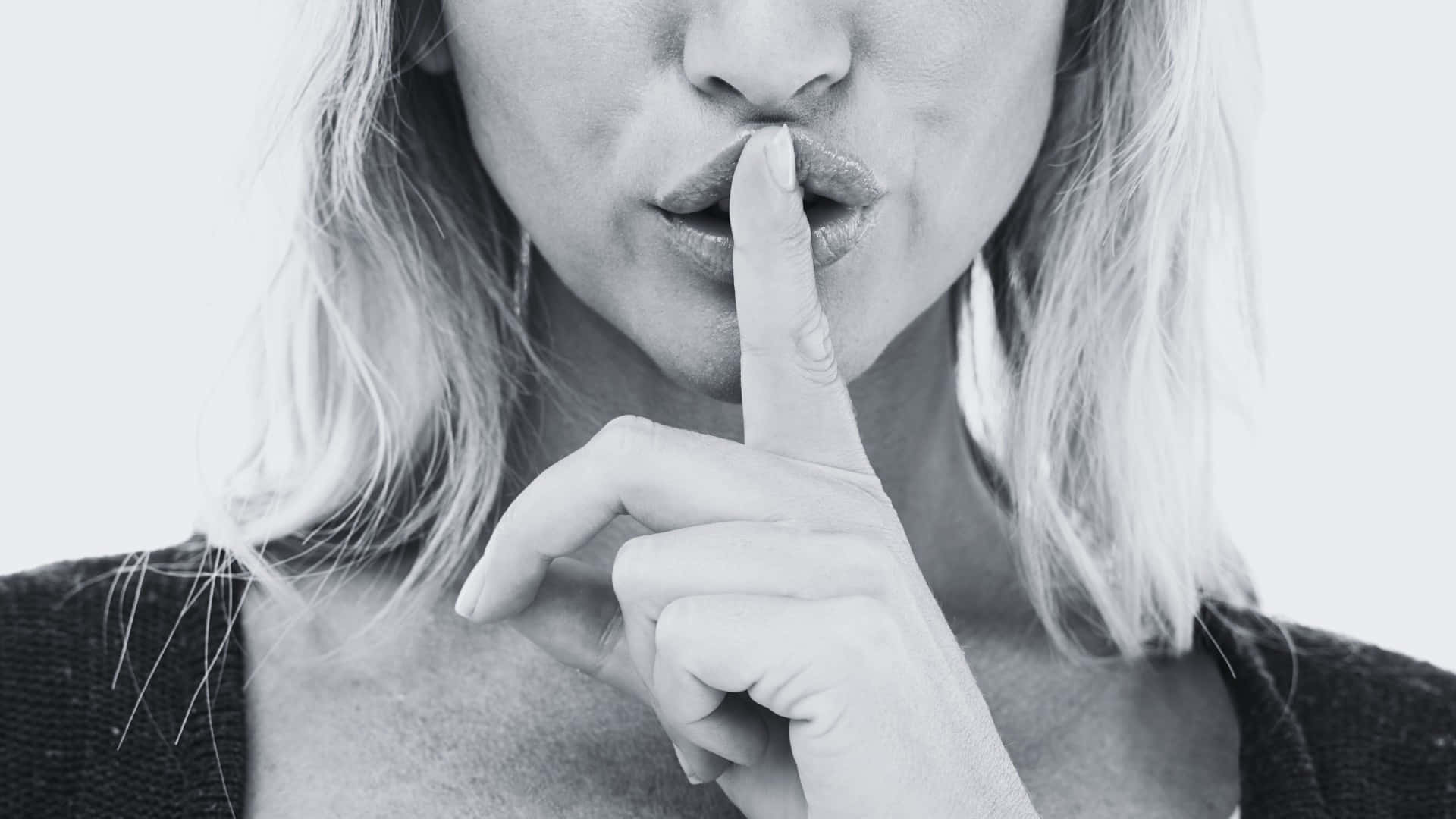  壁紙 — 一位金髮女性在純色背景前將手指放在唇邊做出安靜的手勢。