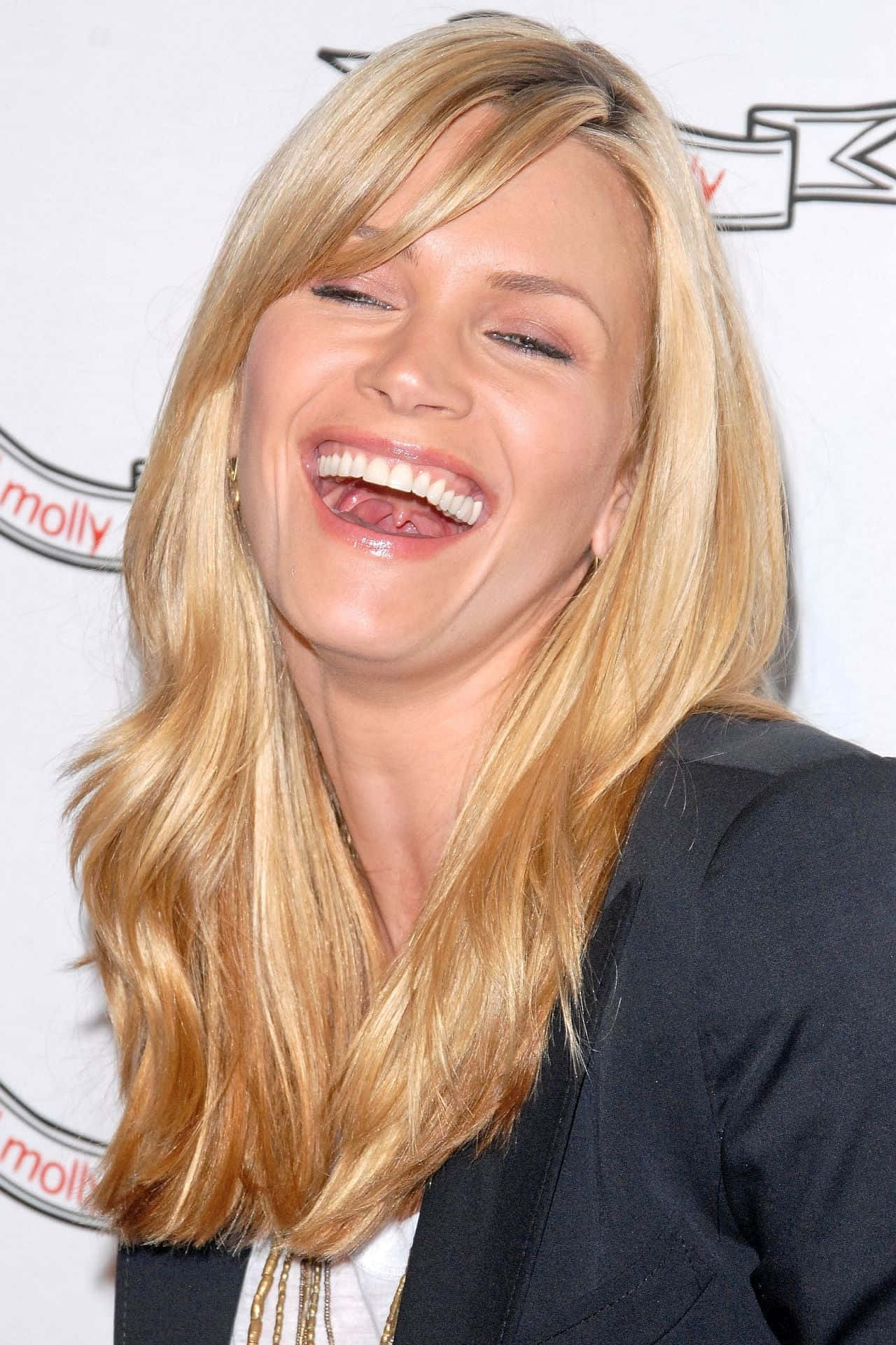 Natasha Henstridge 桌布 壁紙 — 一位金髮女性在品牌背景前開心大笑的近距離肖像。