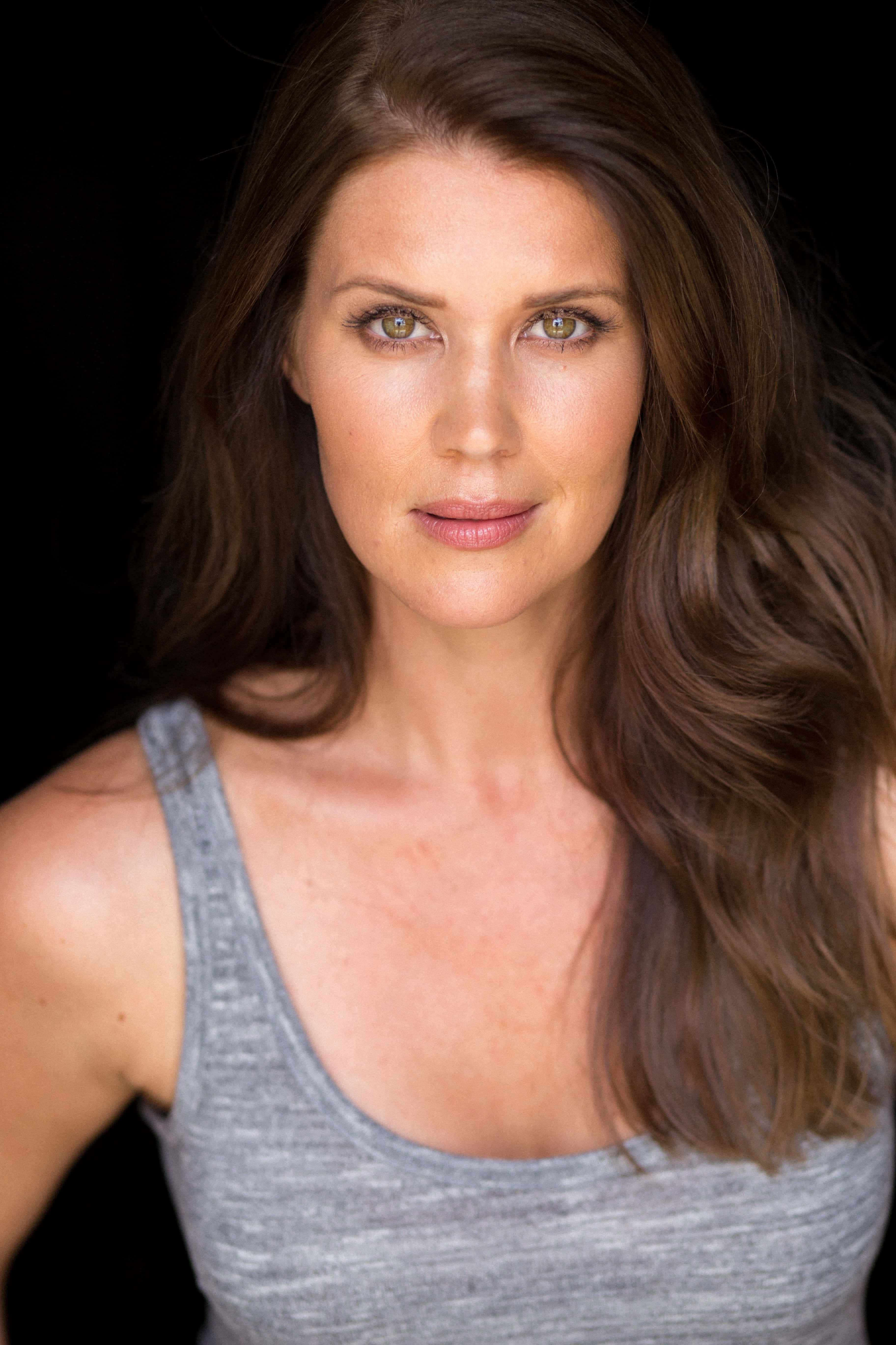 Sarah Lancaster 桌布 壁紙 — 一位擁有長長棕色頭髮和綠色眼睛的女性，在黑色背景下穿著灰色背心，直視鏡頭。