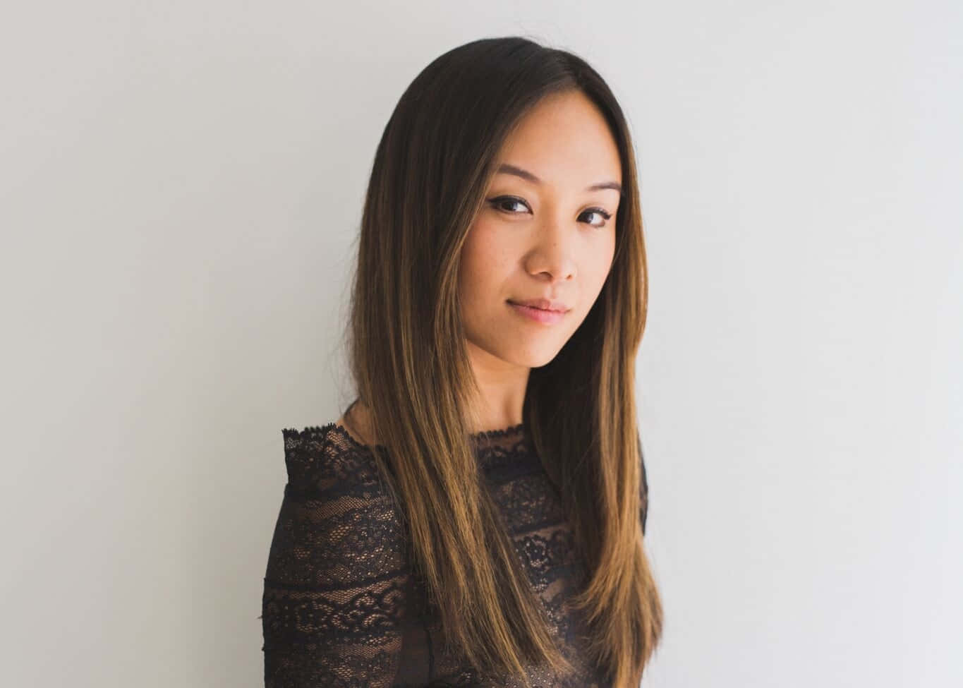  壁紙 — 一位長黑髮女性穿著黑色蕾絲上衣，在純白背景前柔和地擺姿勢。