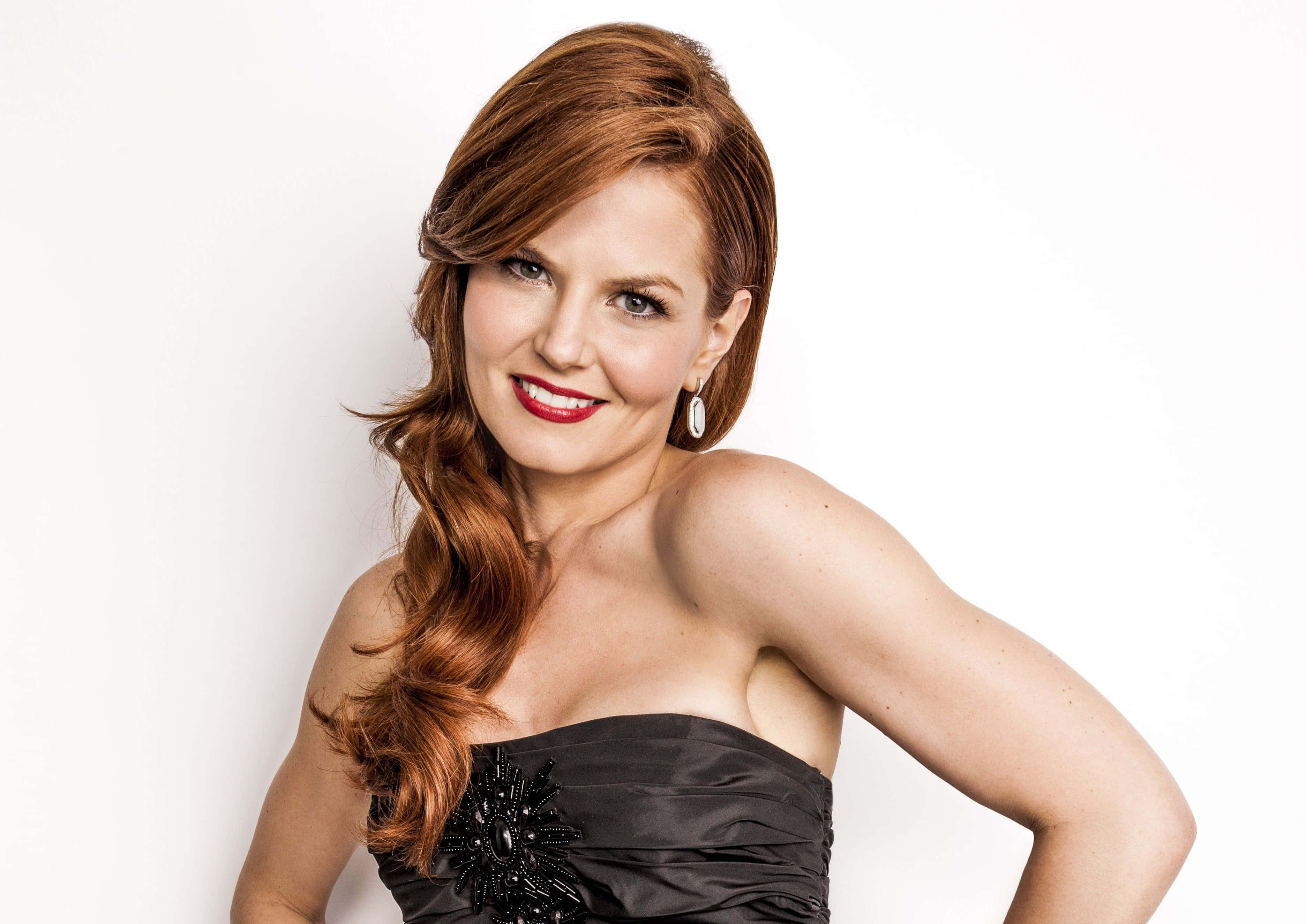 jennifer morrison 桌布 壁紙 — 一位紅髮、塗著鮮紅色唇膏的女性，穿著黑色無肩帶連衣裙，在純白色背景前自信地微笑。